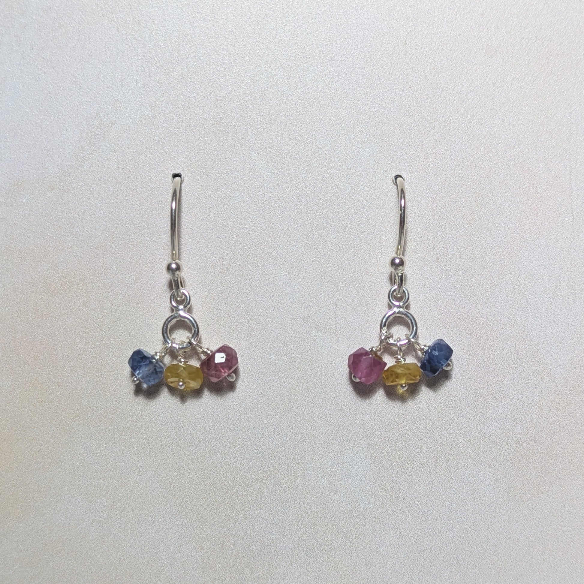 Pair of silver earrings with multicoloured Sapphire gemstone drops on a white background.