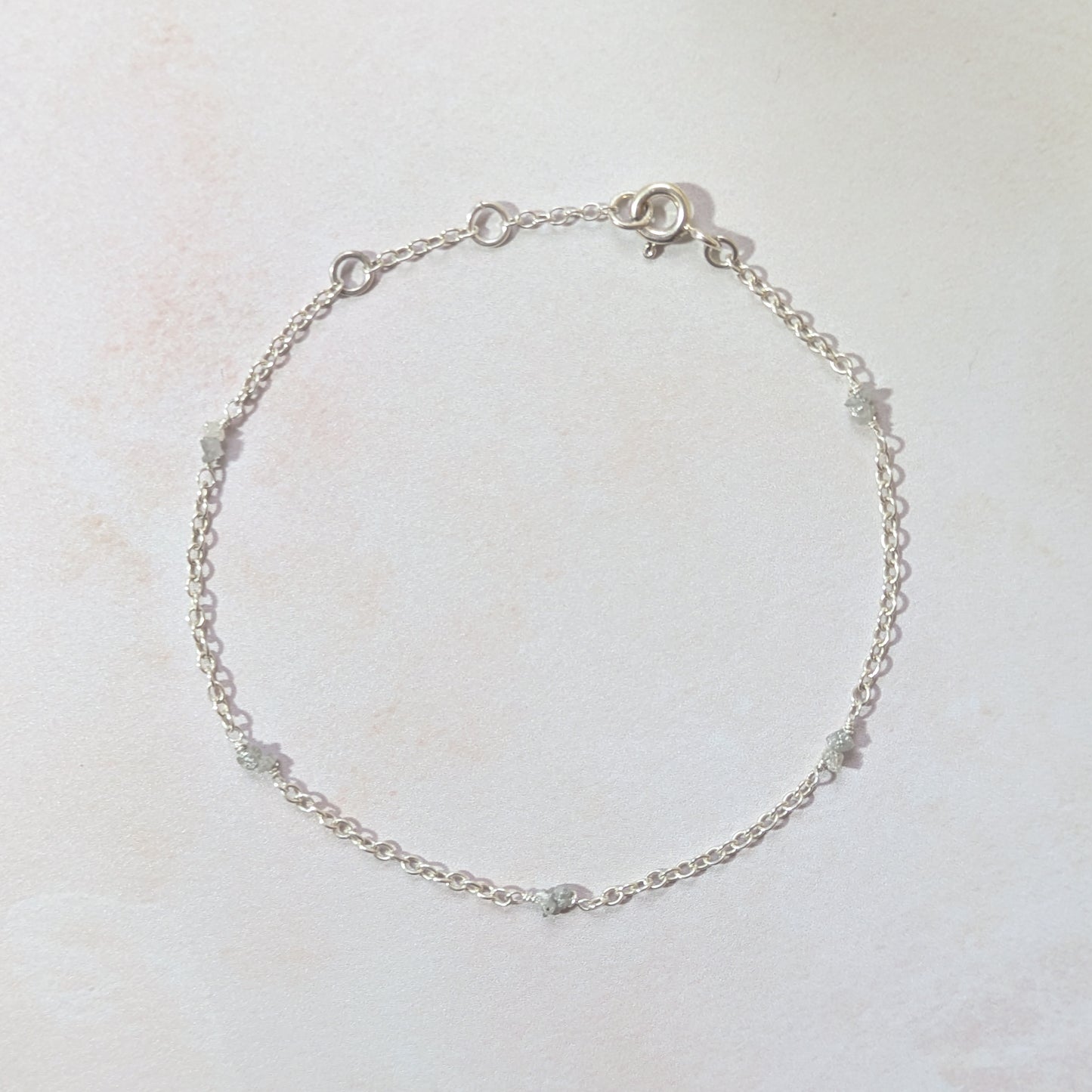 Silver chain bracelet with rough Diamond nuggets on a light beige background.