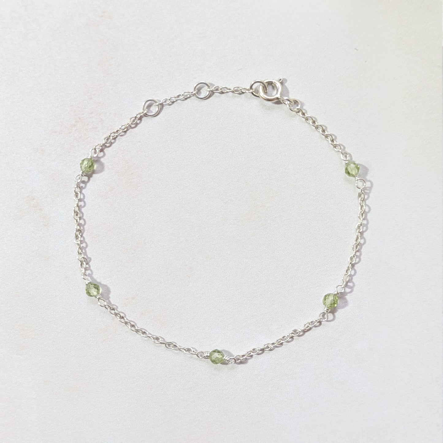 Silver chain bracelet with apple green Peridot gemstone beads on a light background.