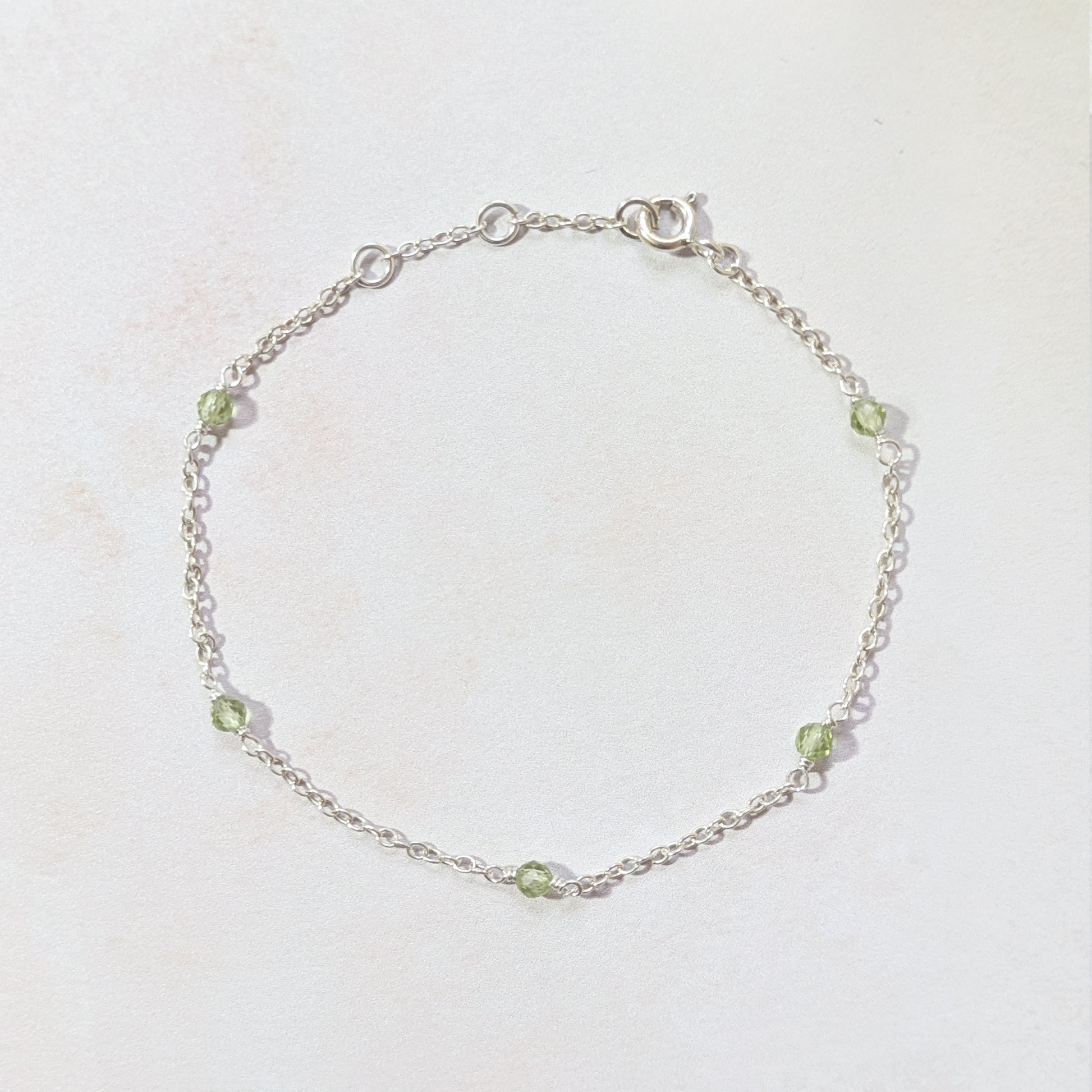 Silver chain bracelet with apple green Peridot gemstone beads on a light background.