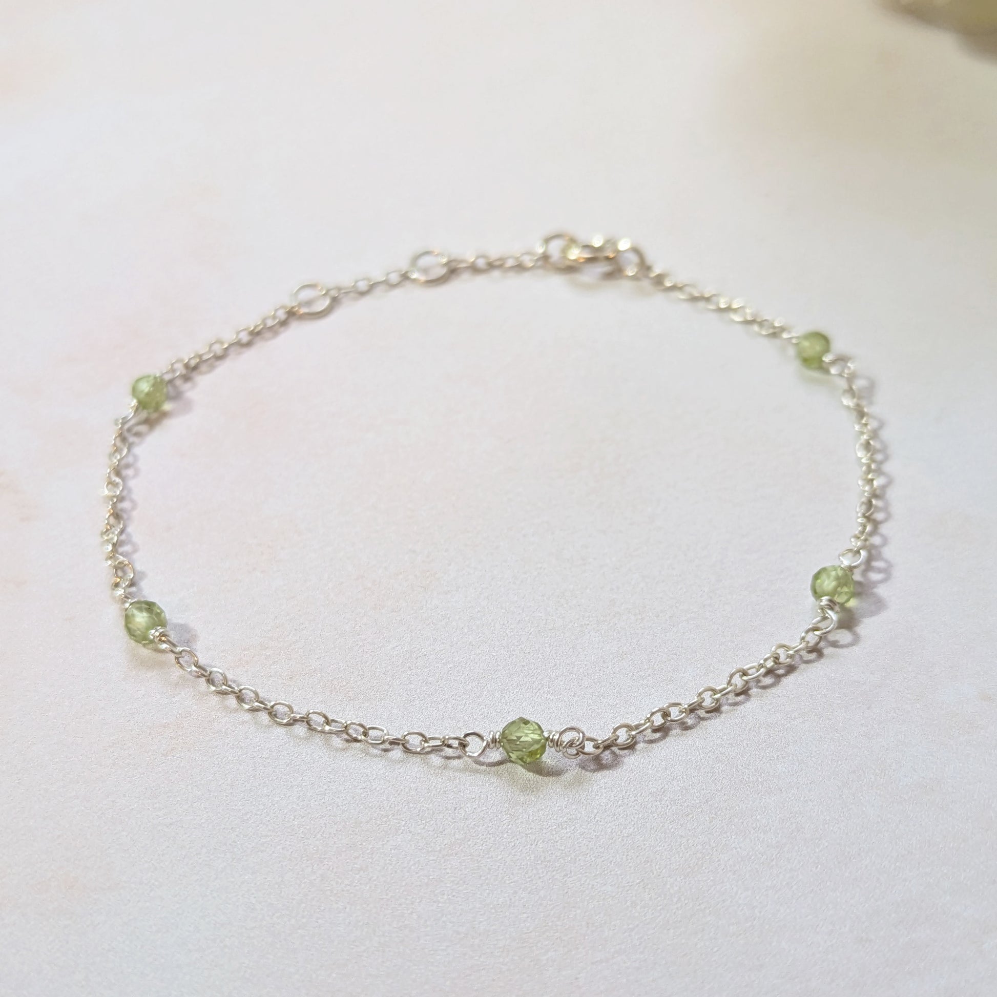 Silver station bracelet with Peridot gemstone beads on a white background.