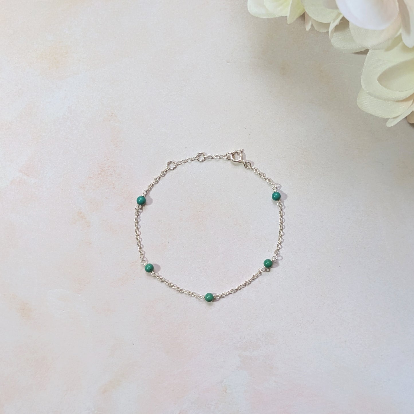 Silver bracelet with natural Turquoise gemstone beads on a light marble surface with flowers.