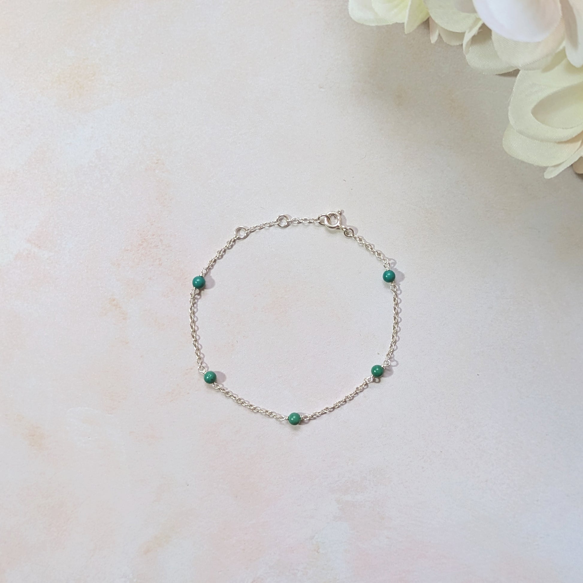 Silver bracelet with natural Turquoise gemstone beads on a light marble surface with flowers.