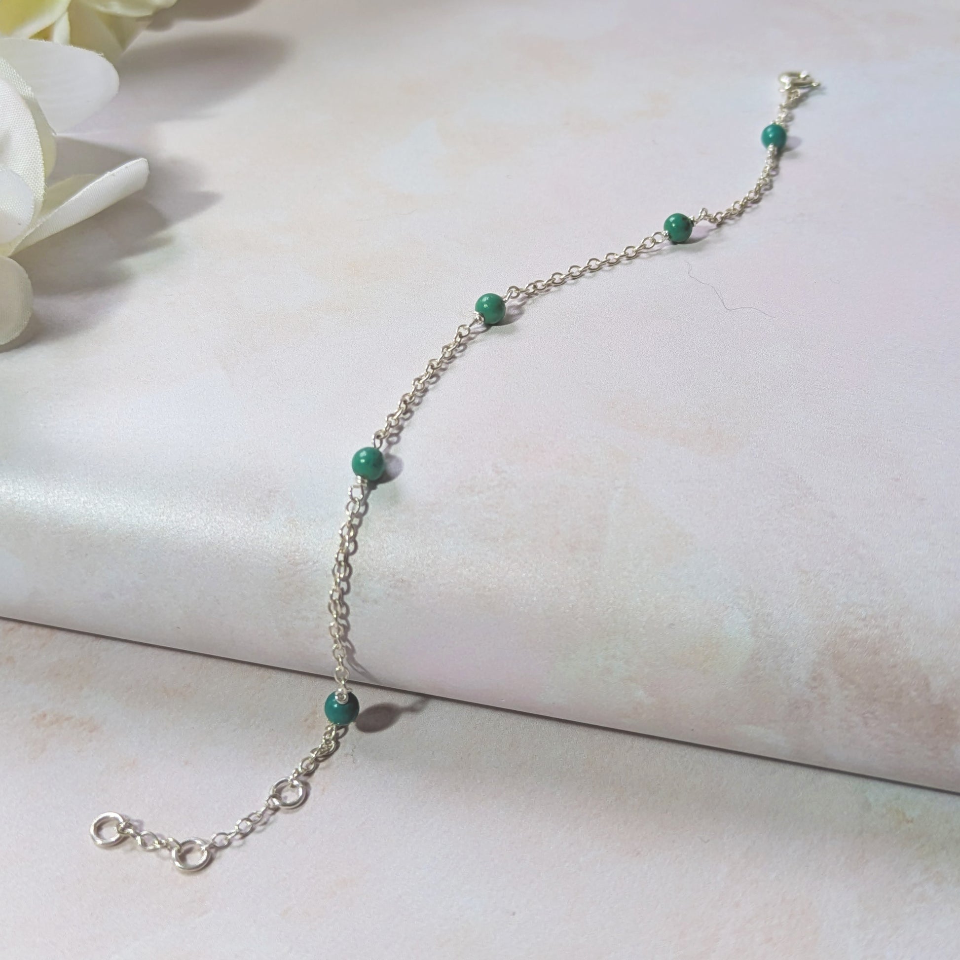 Silver station bracelet with natural Arizona Turquoise gemstone beads on a neutral background with flowers.