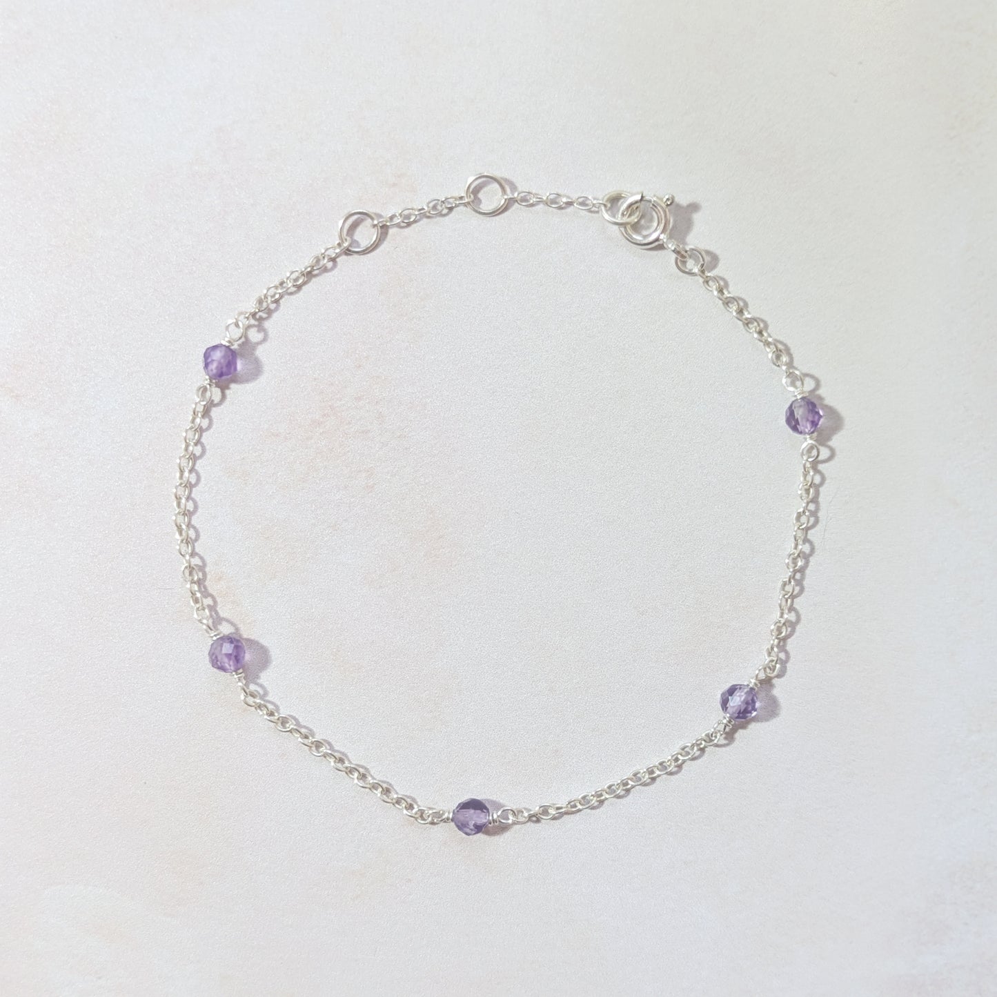 Silver bracelet with purple Amethyst gemstone beads on a white background.