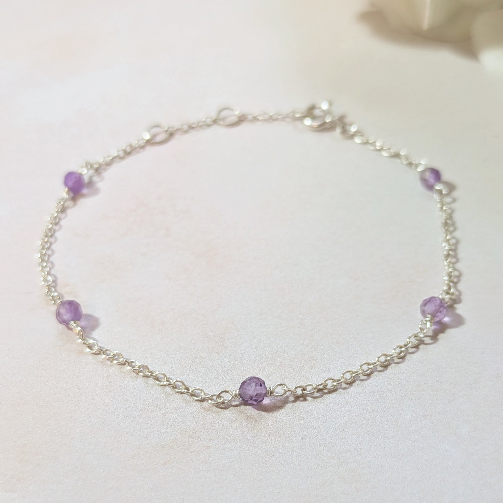Silver chain bracelet with Amethyst gemstone beads on a white background.