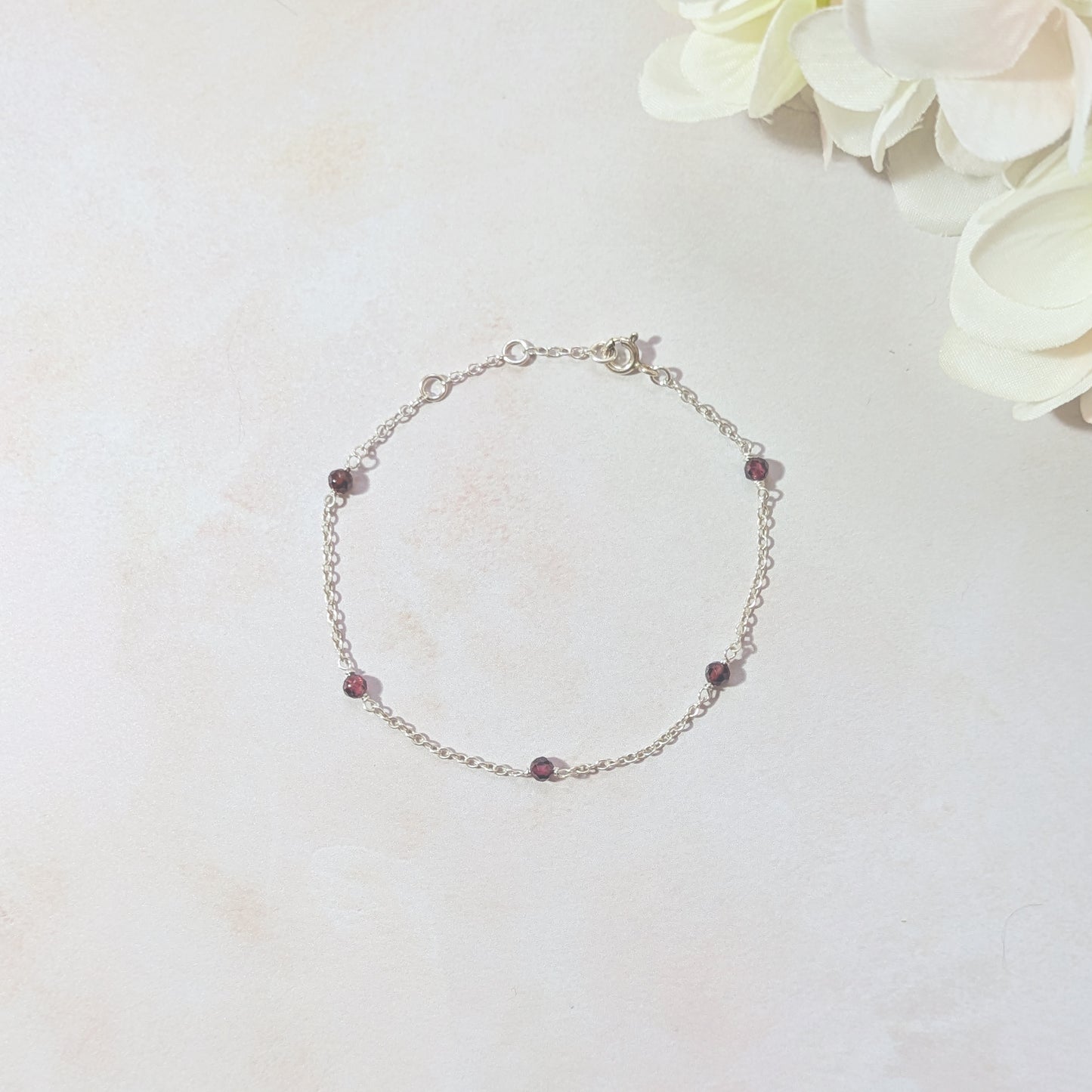 Silver chain bracelet with Garnet gemstone beads on a light background with flowers.