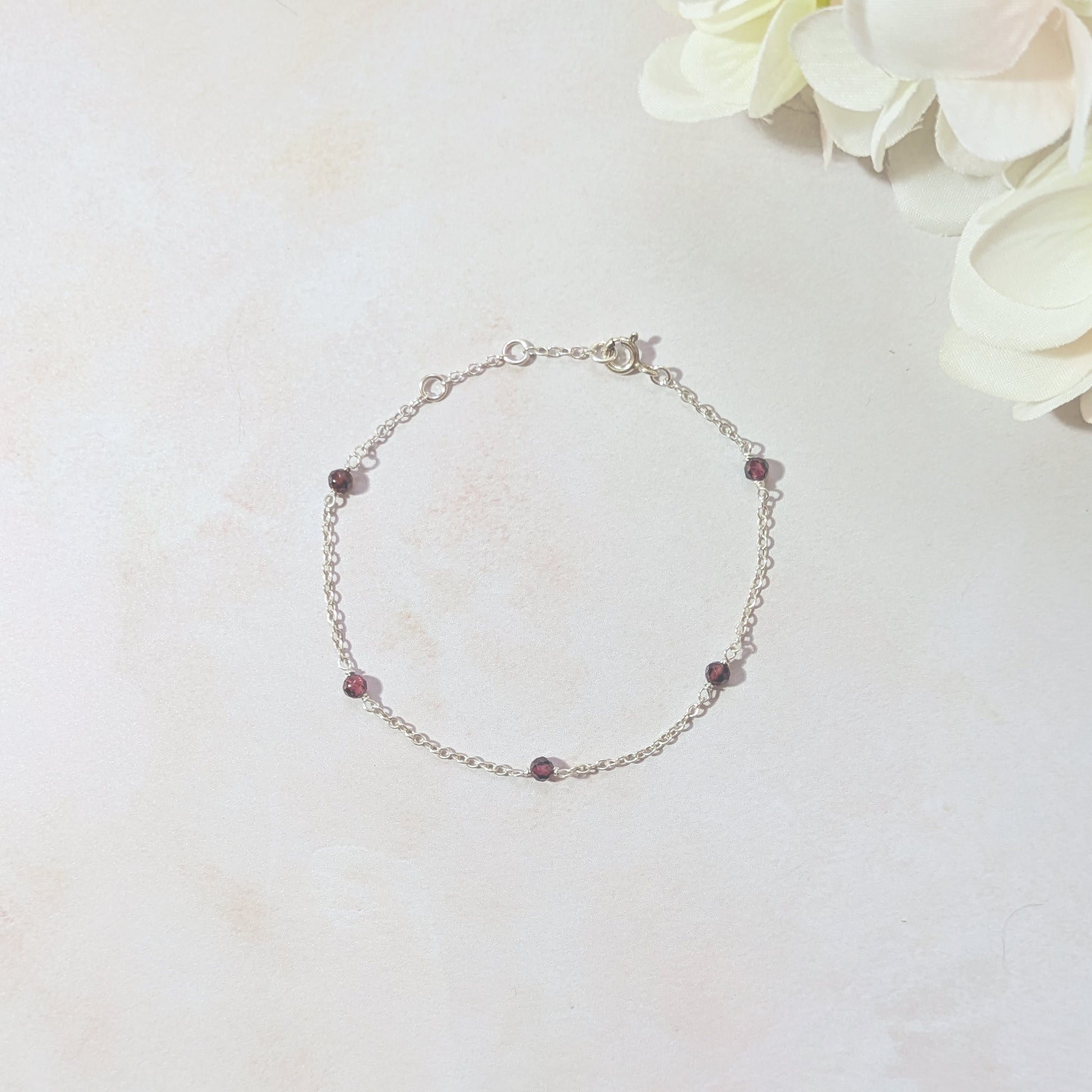 Silver chain bracelet with Garnet gemstone beads on a light background with flowers.