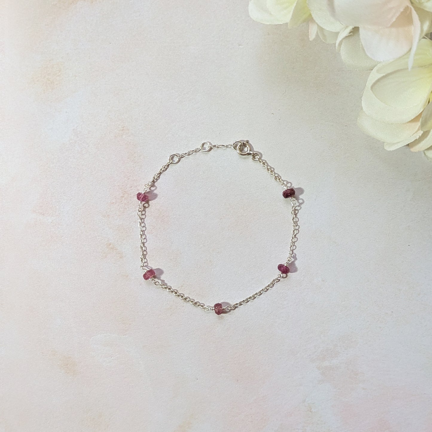 Silver bracelet with Ruby gemstone beads on a light marble background.