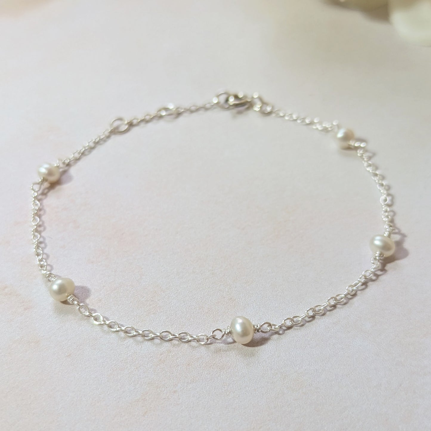 Silver chain bracelet with pearls on a light background.