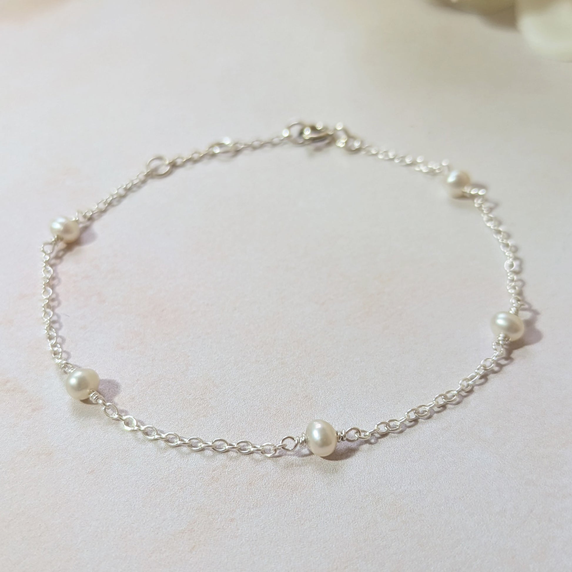 Silver chain bracelet with pearls on a light background.