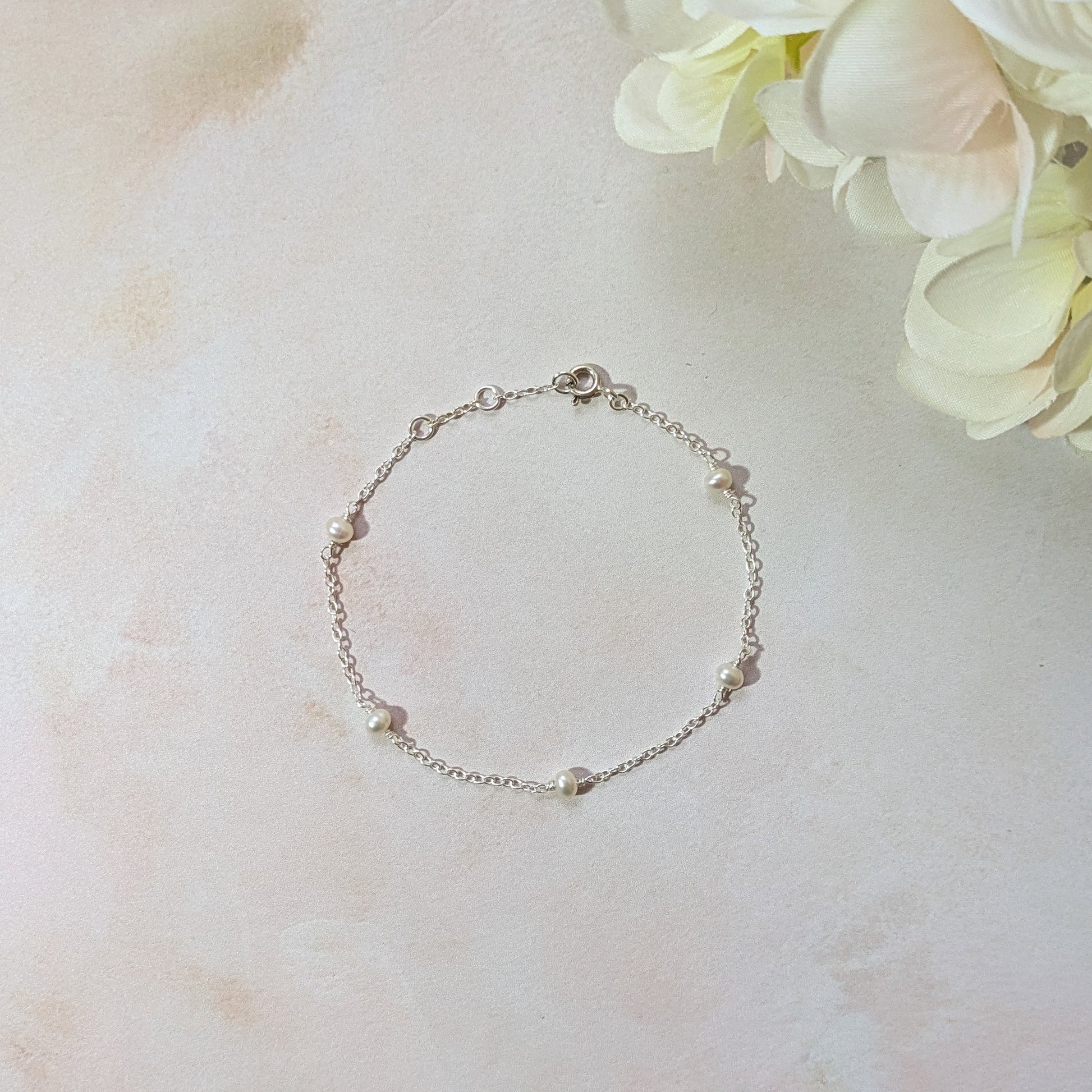 Silver station bracelet with freshwater pearls on a light marble surface with flowers in the background.