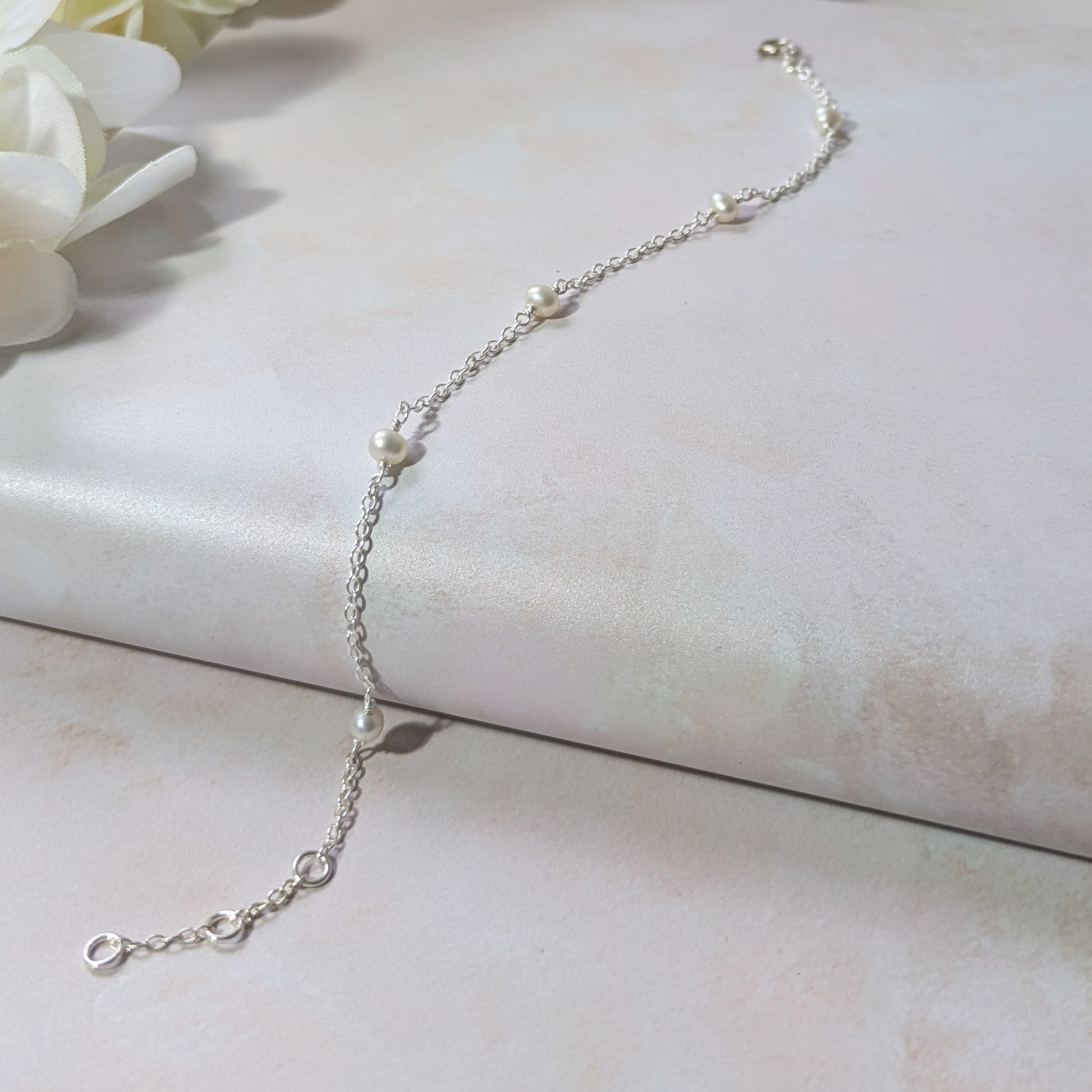 Silver stationed chain bracelet with small pearls on a light surface.