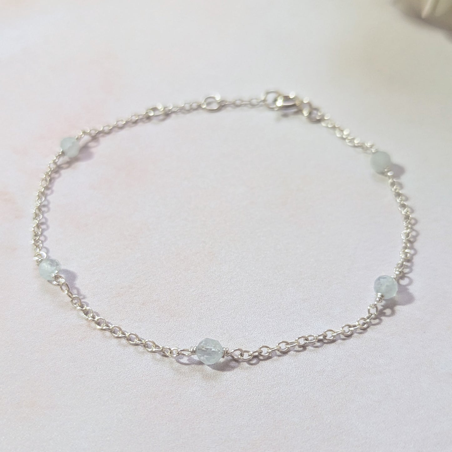 Silver chain bracelet with pale blue Aquamarine gemstone beads on a white background.
