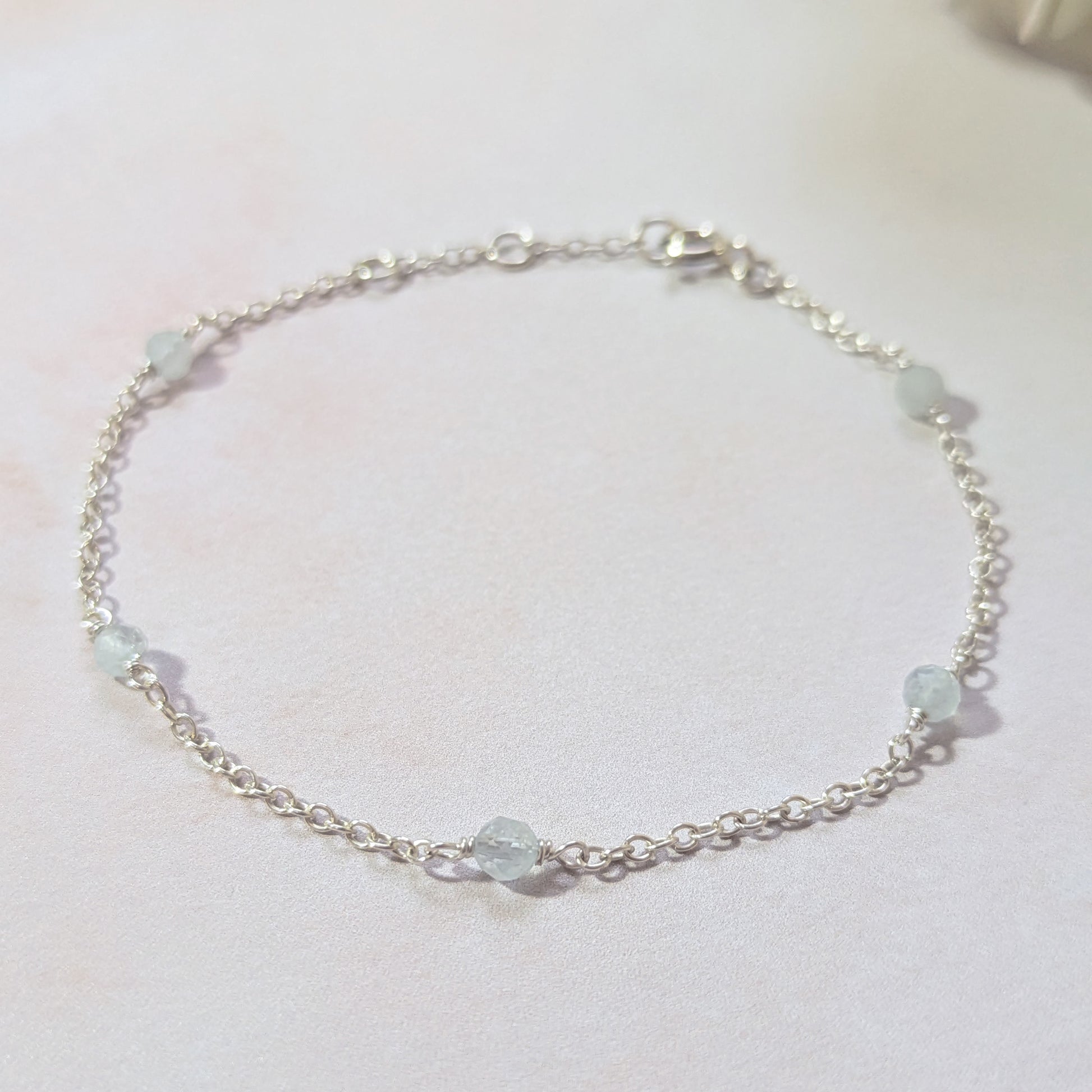 Silver chain bracelet with pale blue Aquamarine gemstone beads on a white background.