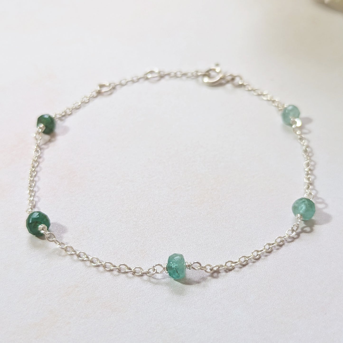Silver station bracelet with green Emerald gemstone beads on a white background.