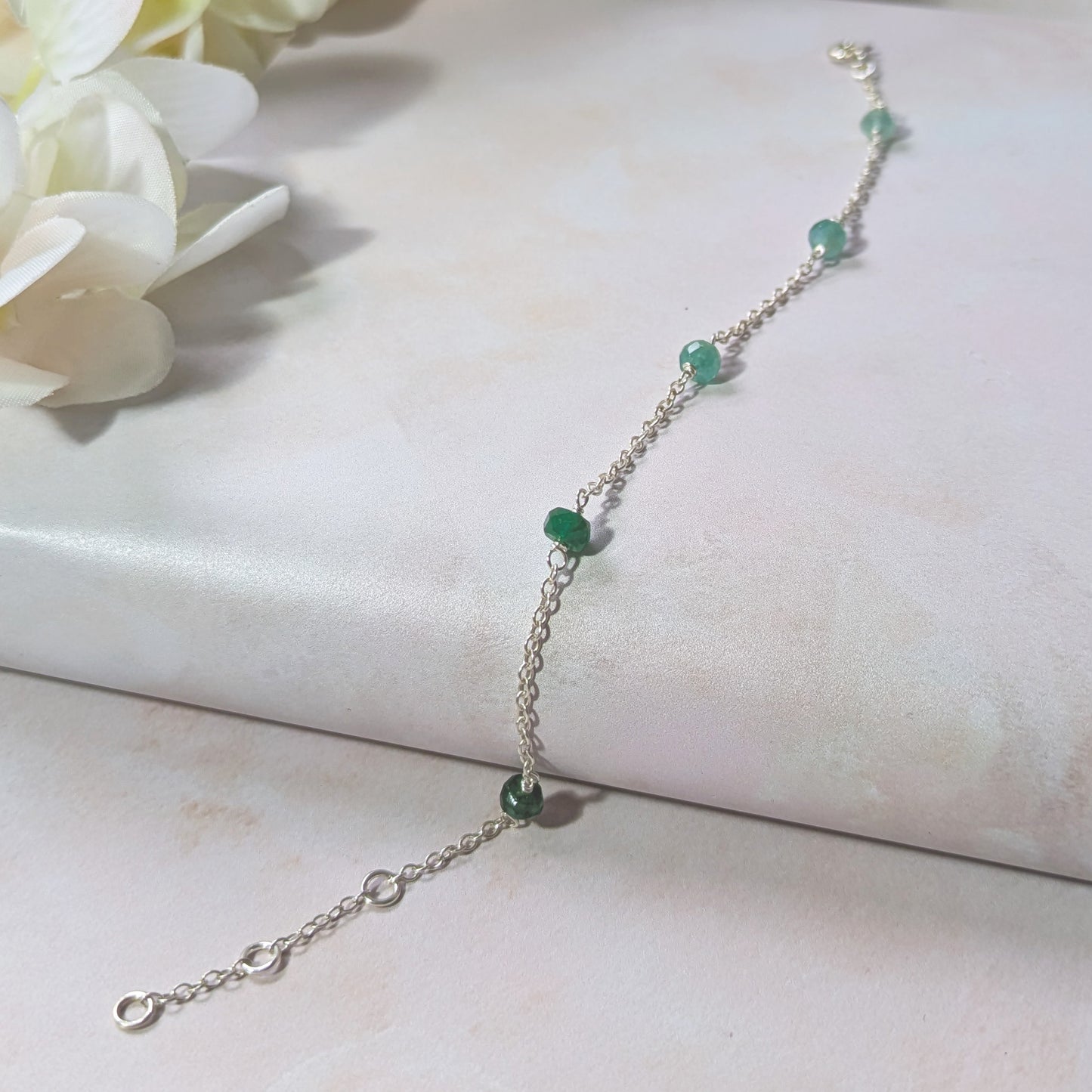 Silver stationed chain bracelet with Emerald gemstone beads on a white surface with flowers.