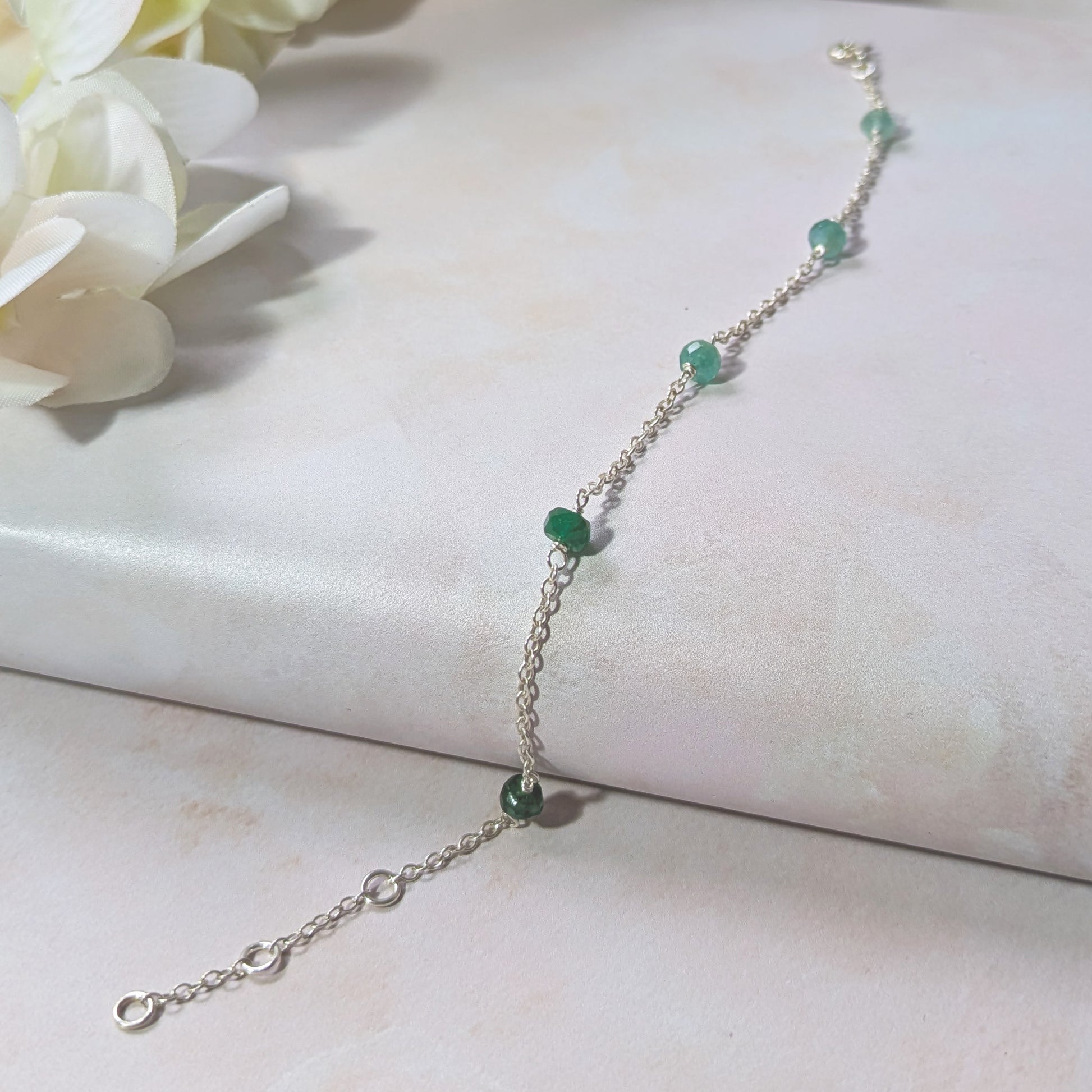 Silver stationed chain bracelet with Emerald gemstone beads on a white surface with flowers.