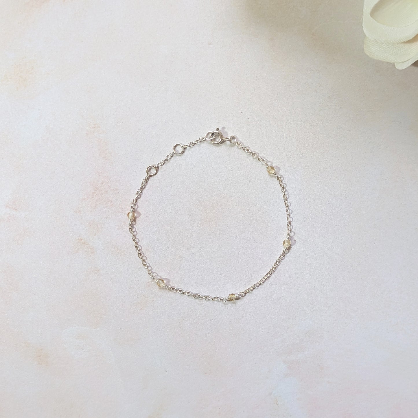 Silver station bracelet with Citrine gemstone beads on a light marble surface with a white flower.