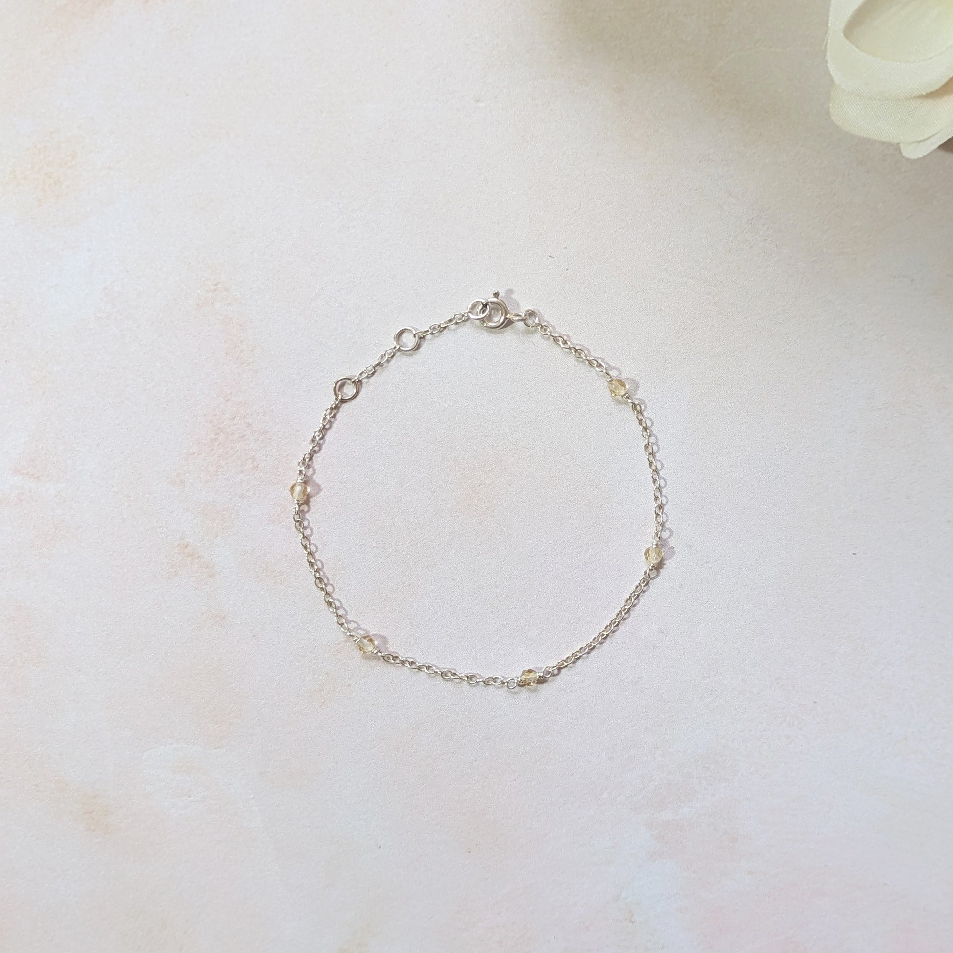 Silver station bracelet with Citrine gemstone beads on a light marble surface with a white flower.
