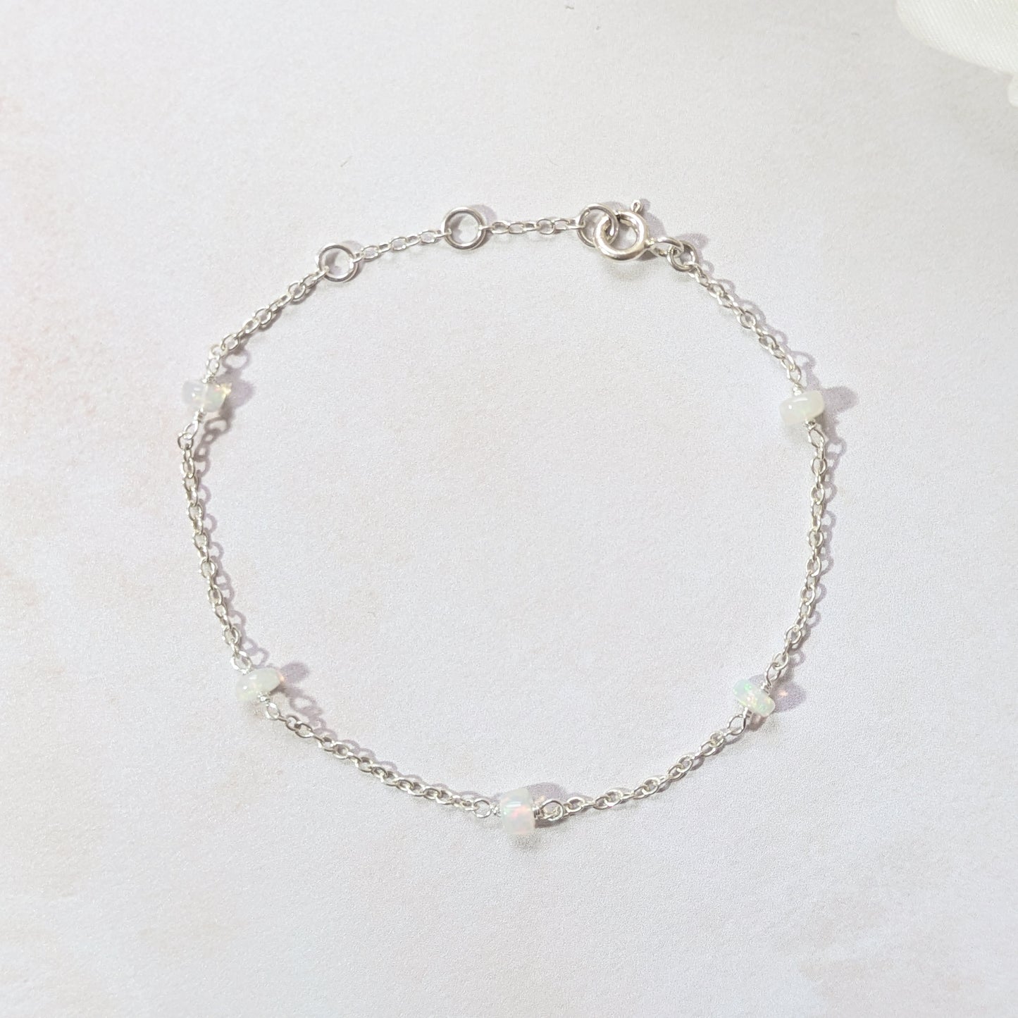 Silver bracelet with Opal gemstone  beads on a light grey background.