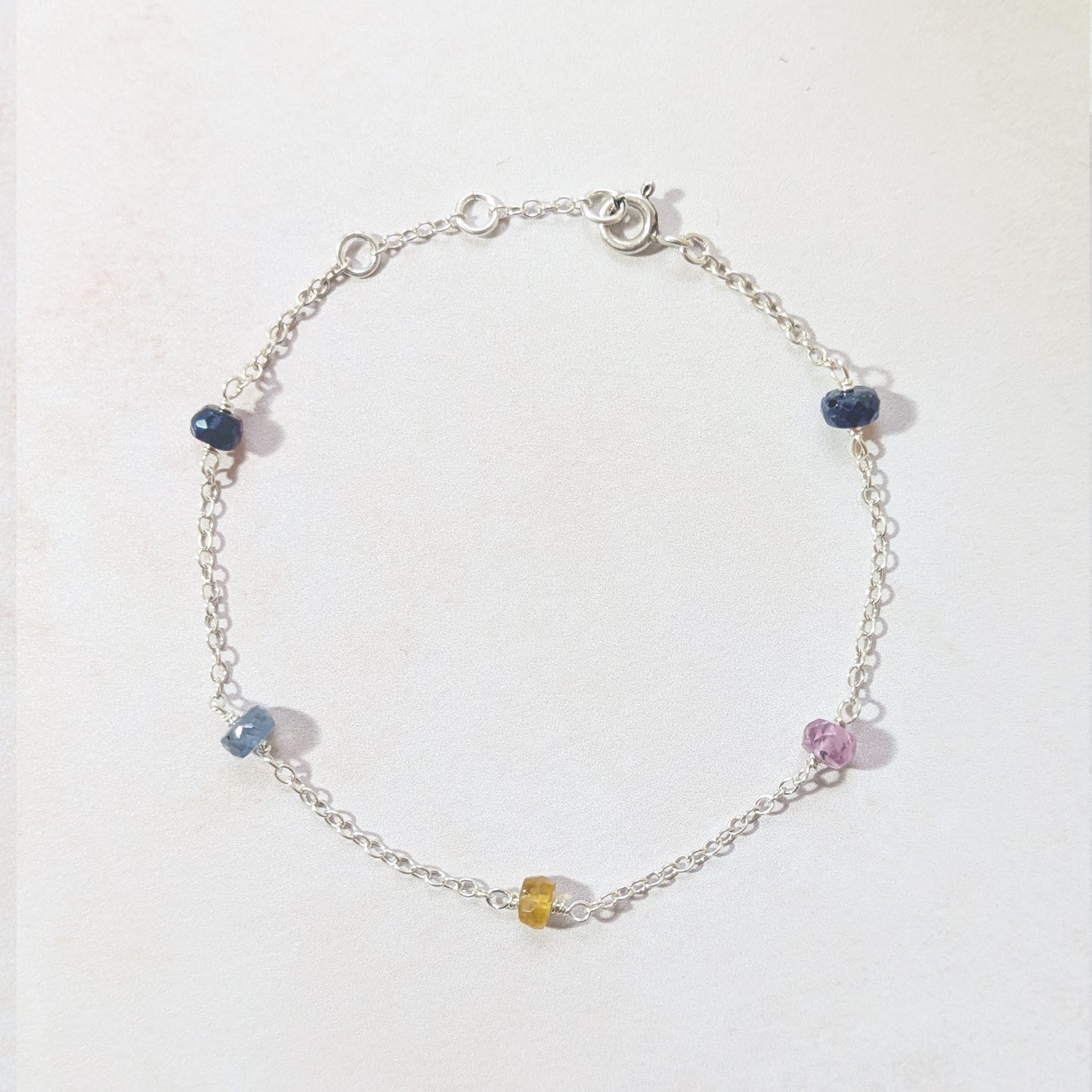 Silver bracelet with multicoloured Sapphire beads on a white background.