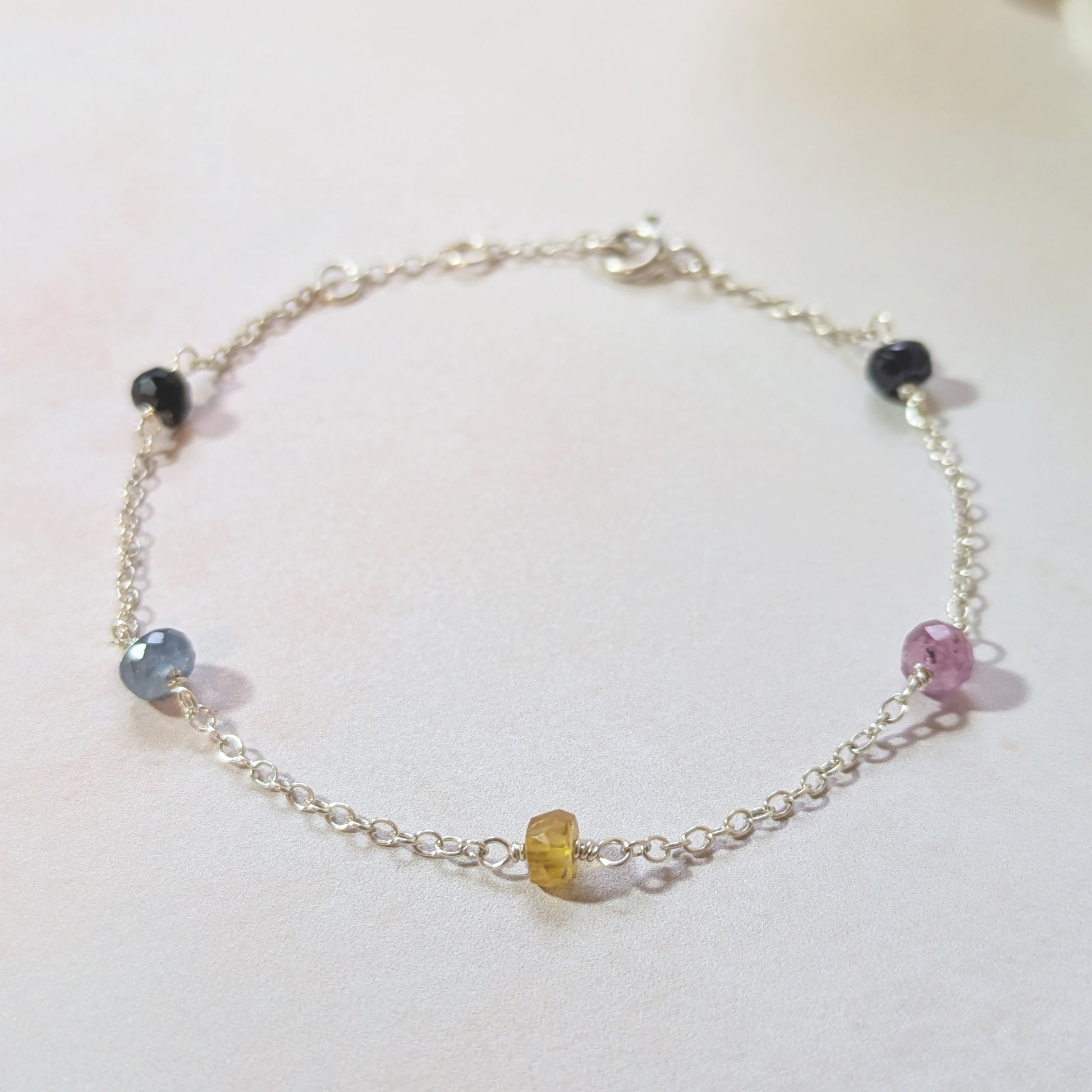 Silver station bracelet with multicoloured Sapphire beads on a light background.