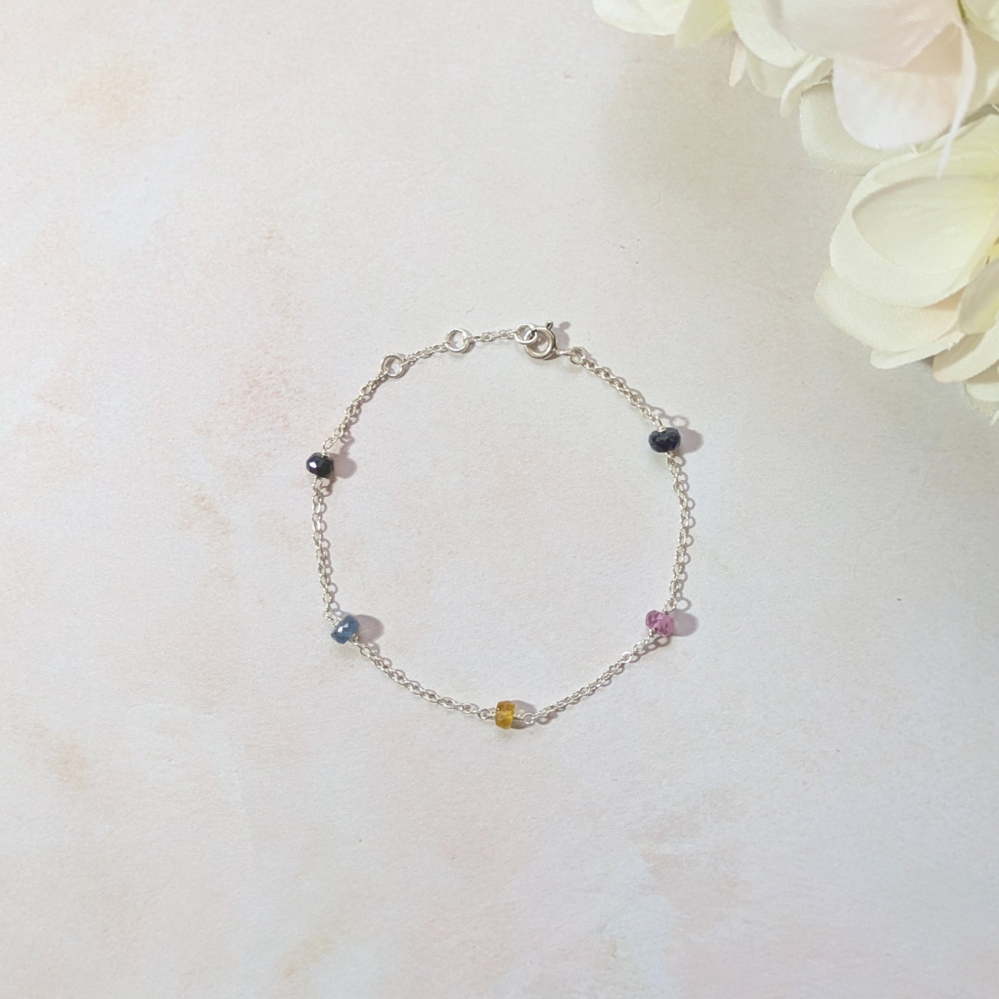 Silver stationed bracelet with blue, pink and yellow Sapphire gemstone beads on a light background.
