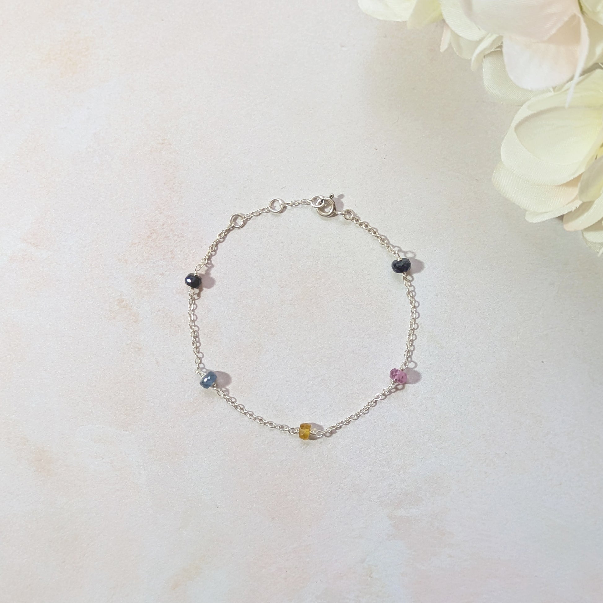 Silver stationed bracelet with blue, pink and yellow Sapphire gemstone beads on a light background.