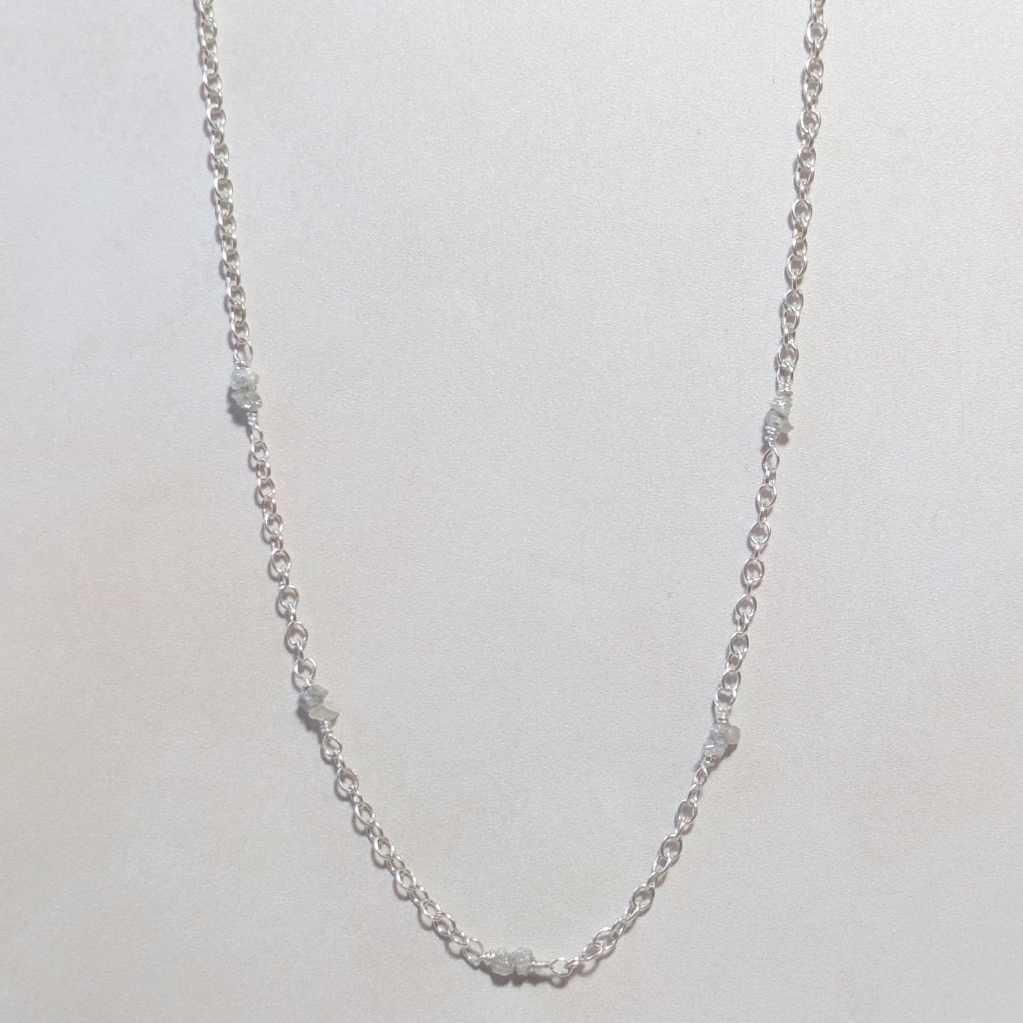Silver chain necklace with rough Diamond nuggets on a light neutral background.