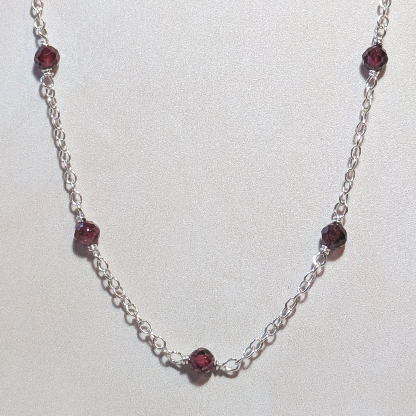 Silver necklace with Garnet gemstone beads on a white background.