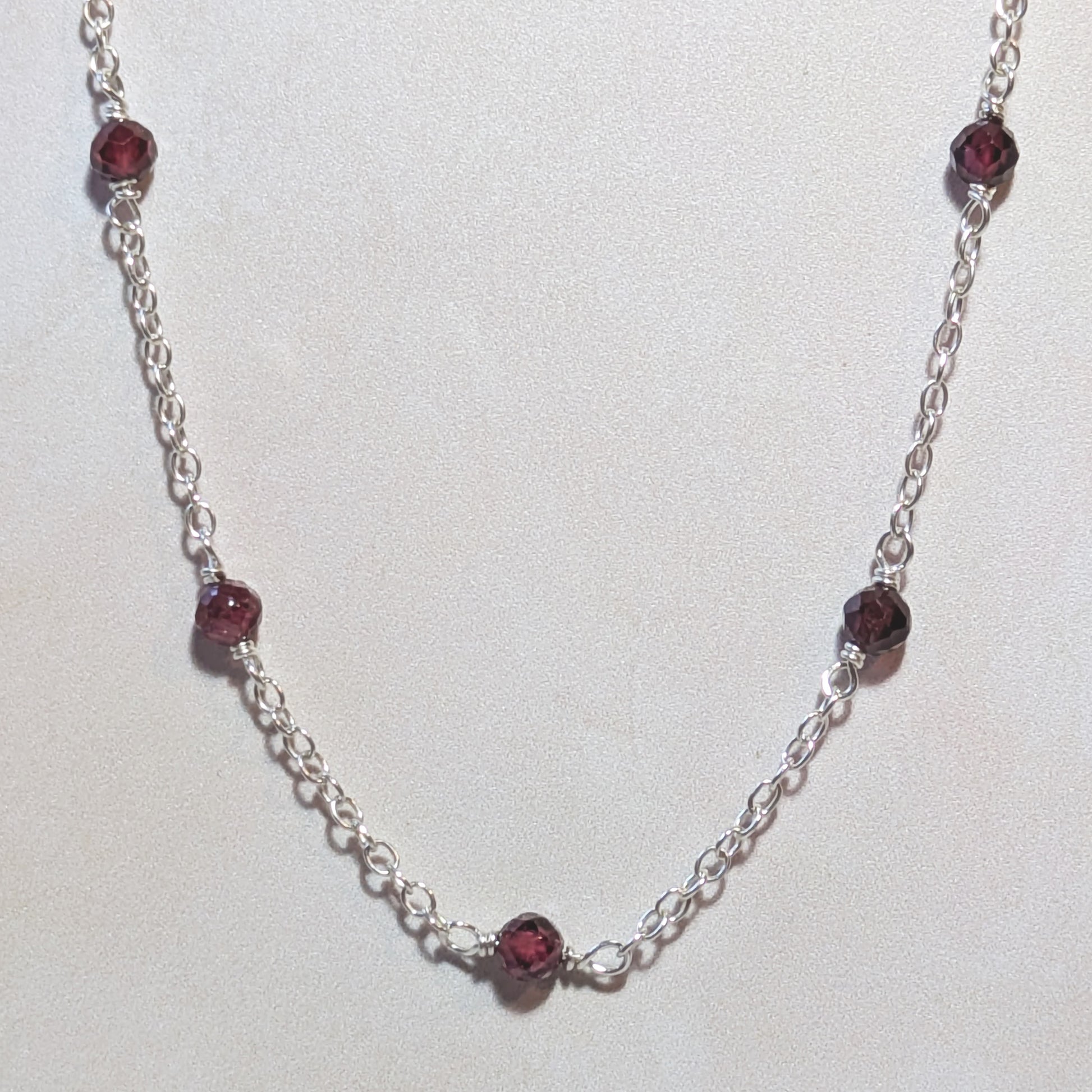 Silver necklace with Garnet gemstone beads on a white background.