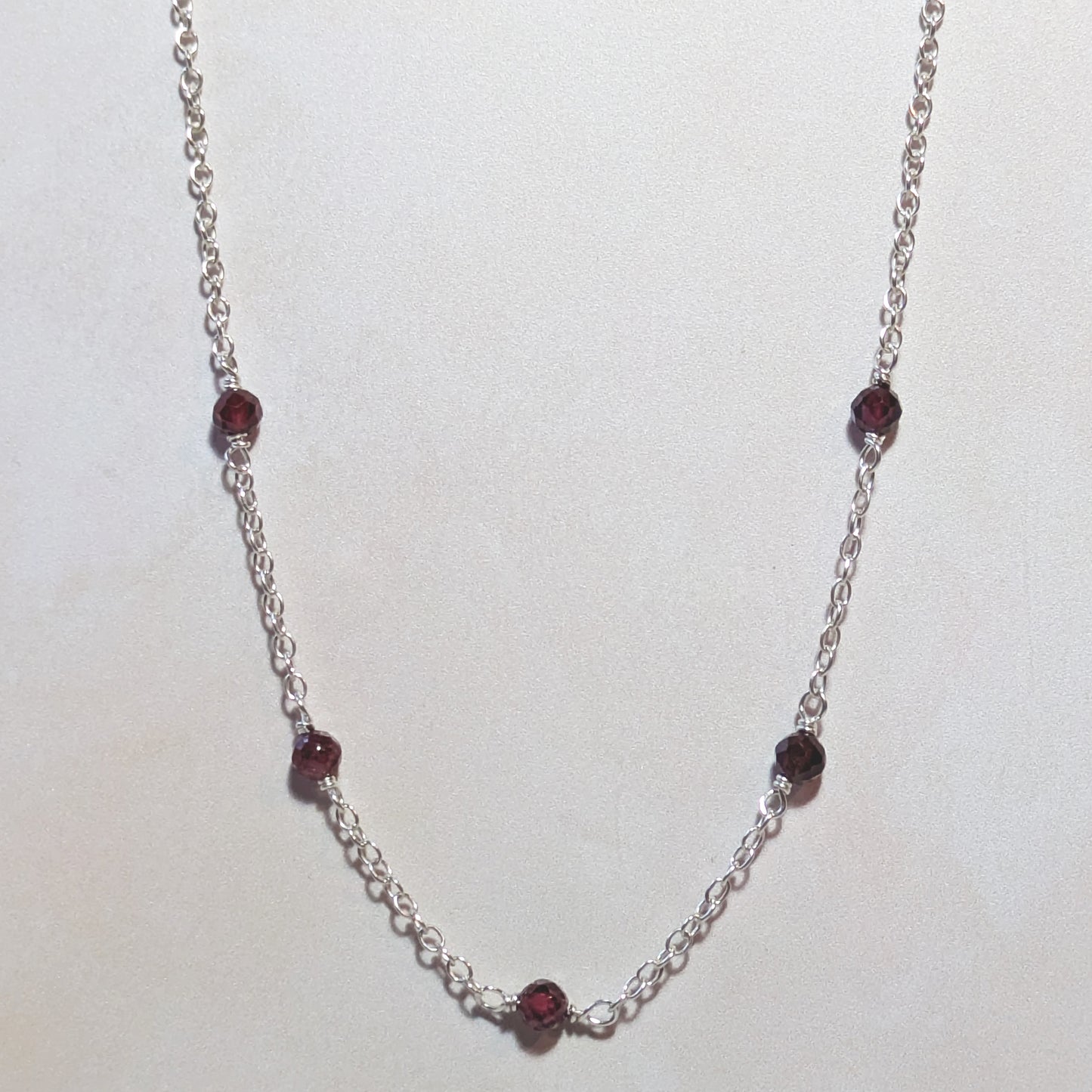 Silver chain necklace with red Garnet gemstones on a white background.