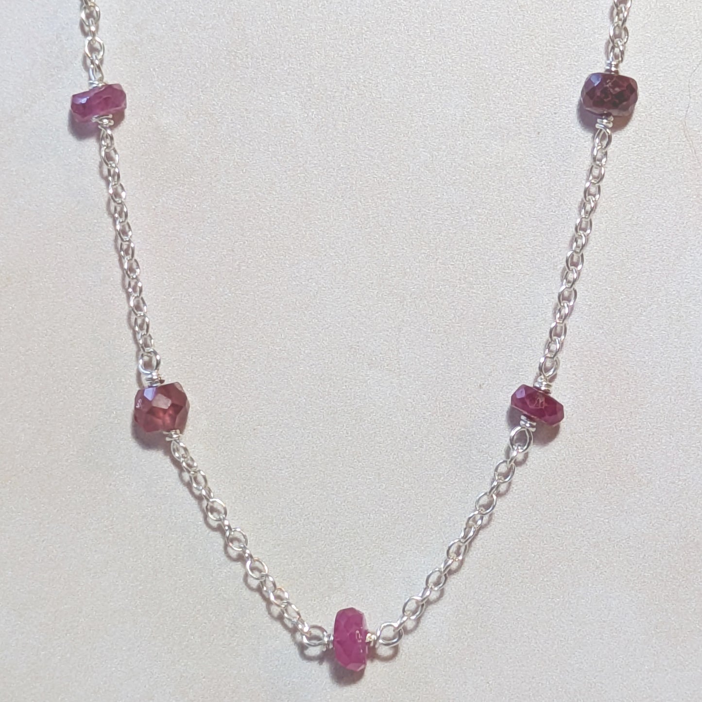 Silver necklace with Ruby gemstone beads on a white background.