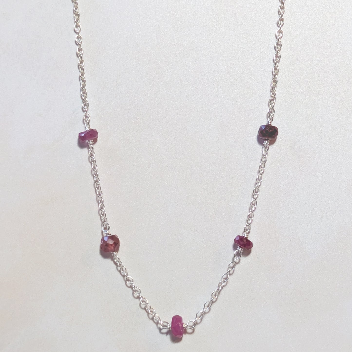 Silver chain necklace with Ruby gemstone beads on a white background.