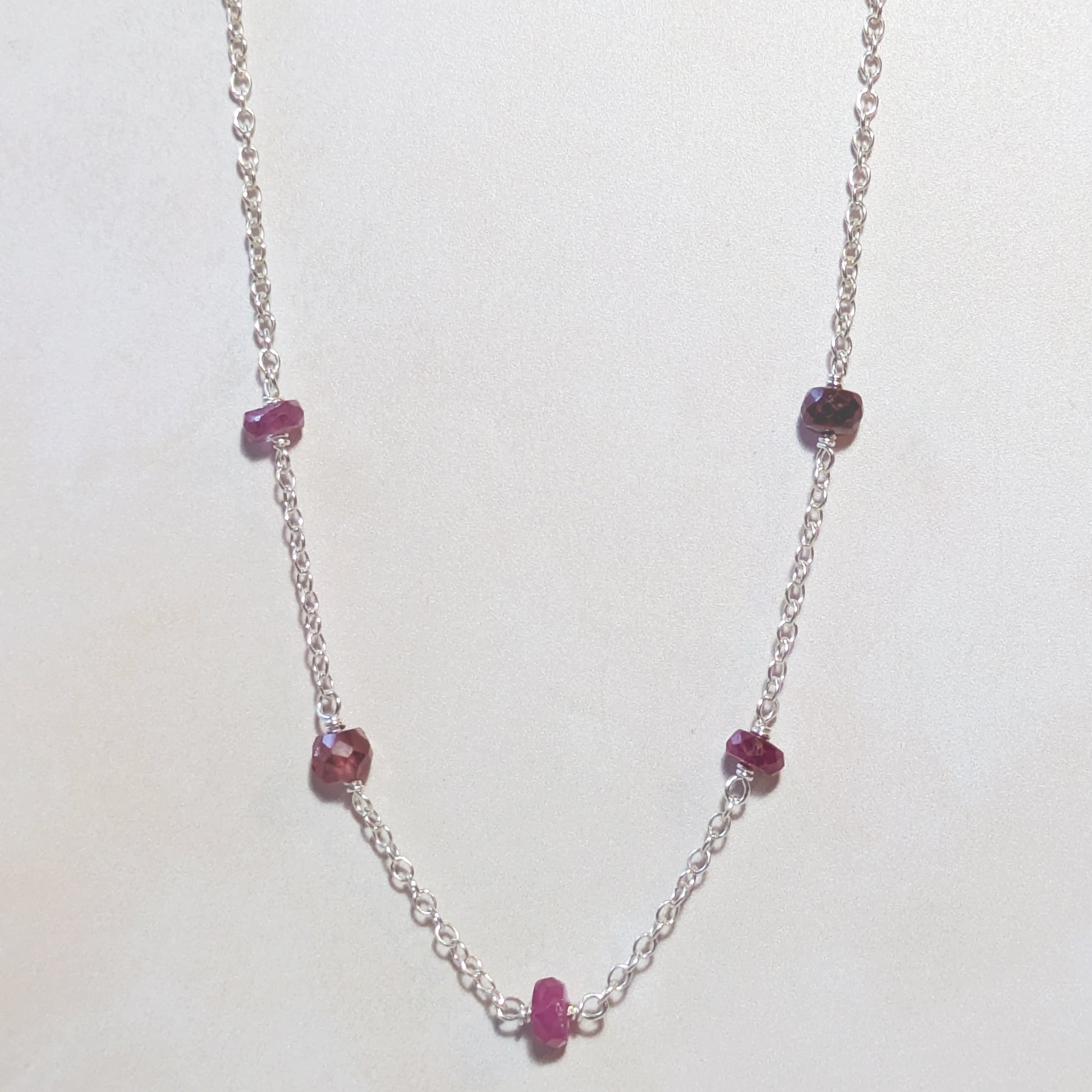 Silver chain necklace with Ruby gemstone beads on a white background.