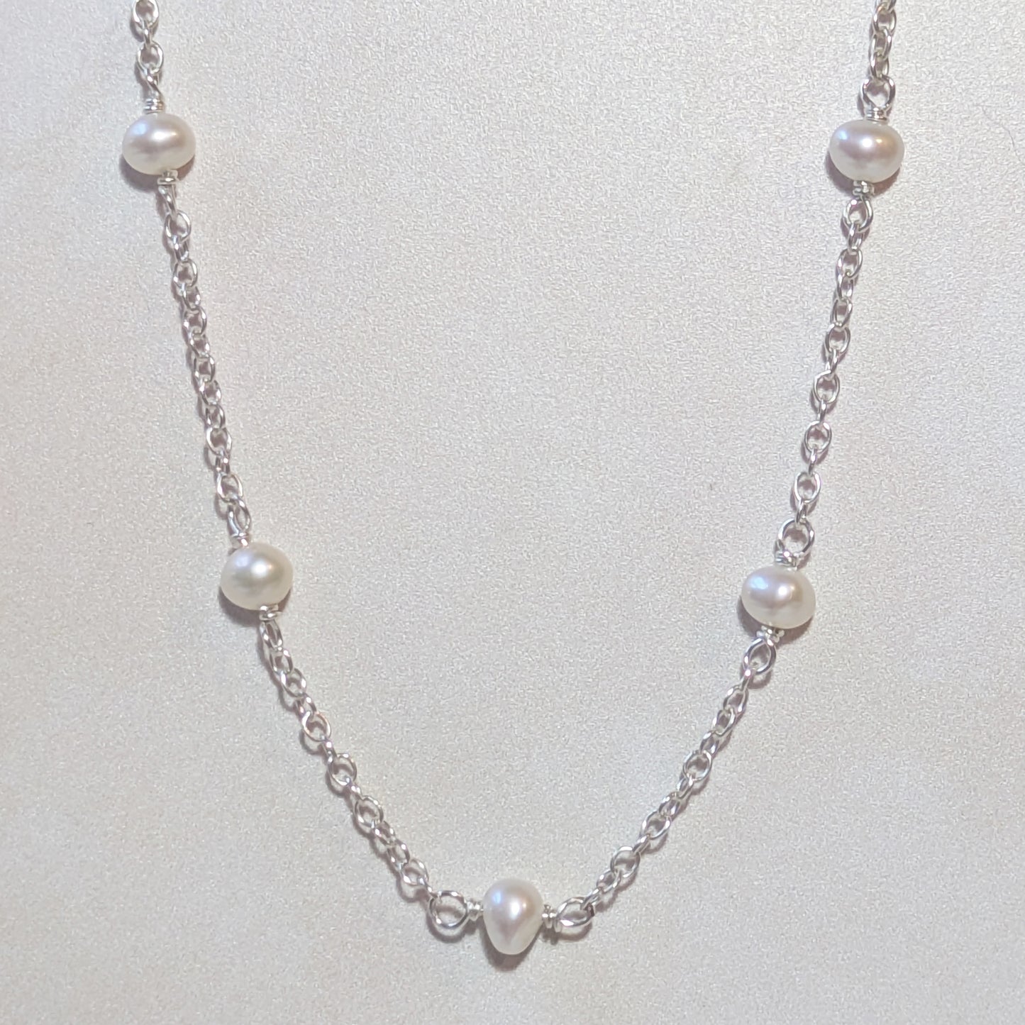 Pearl necklace with silver chain on a light grey background.