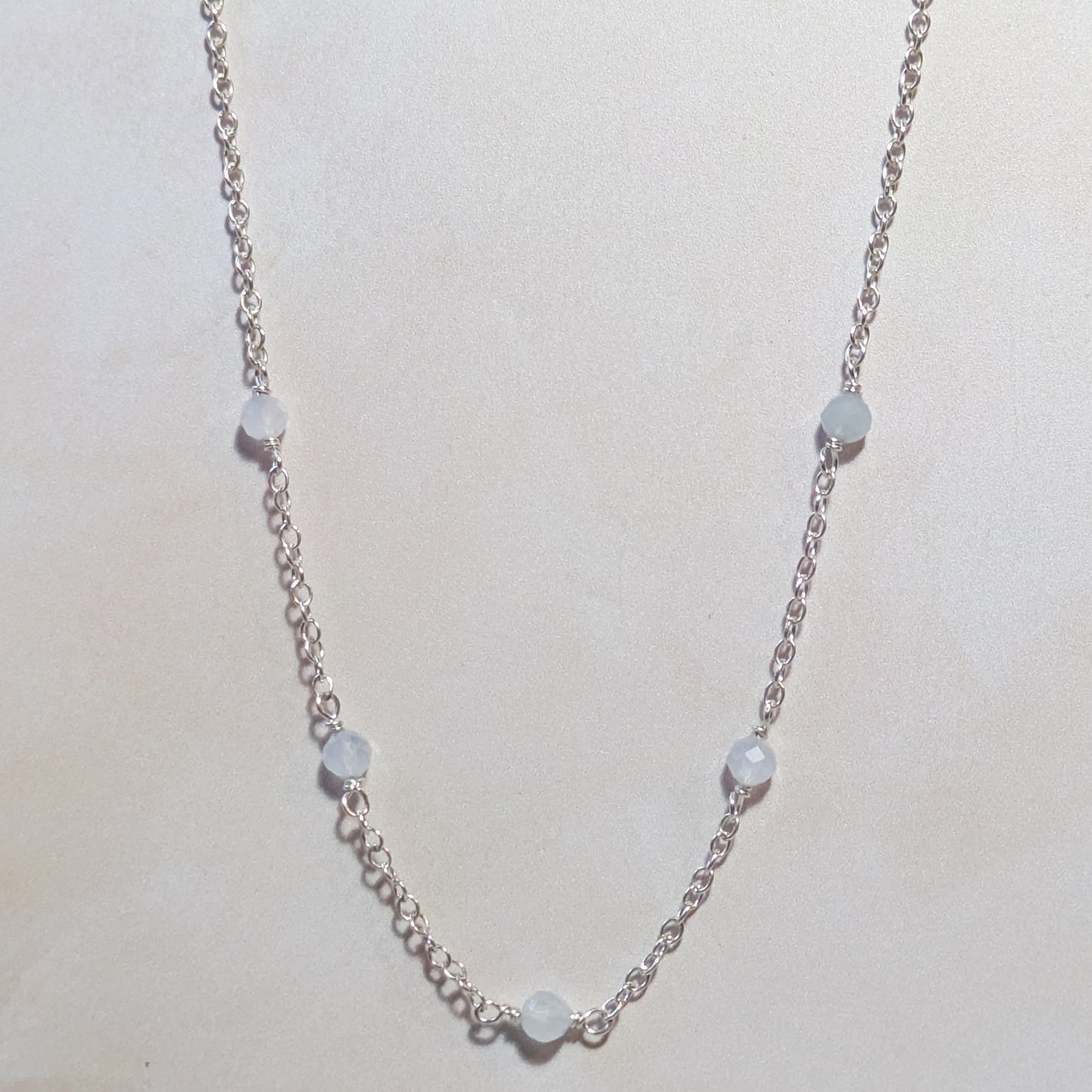 Silver necklace with small round Aquamarine beads on a pale neutral background.