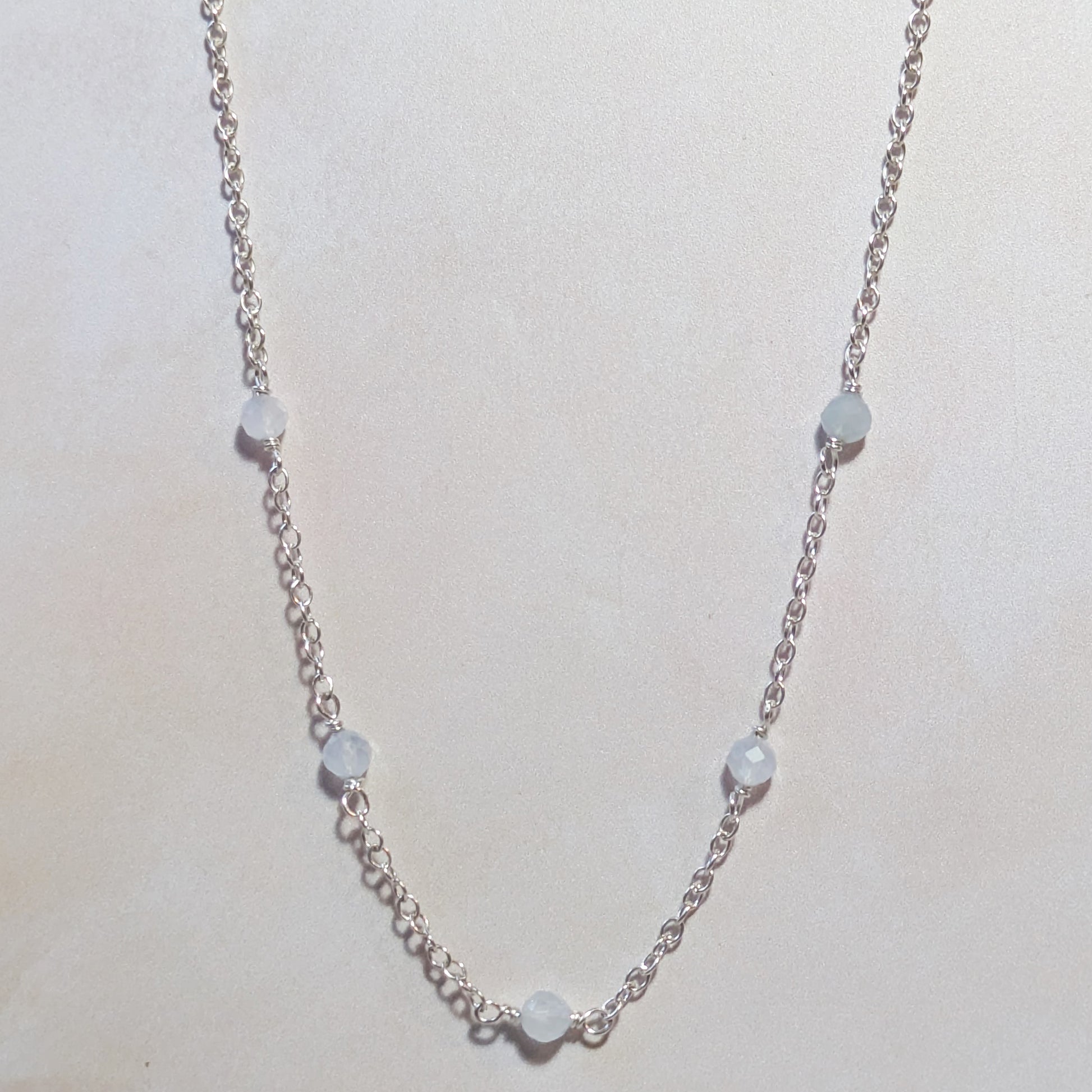 Silver necklace with small round Aquamarine beads on a pale neutral background.