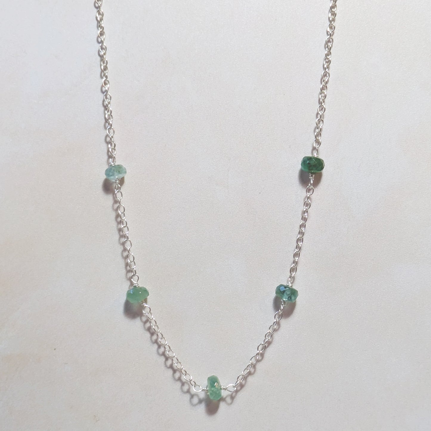 Silver necklace with green Emerald gemstones on a white background.