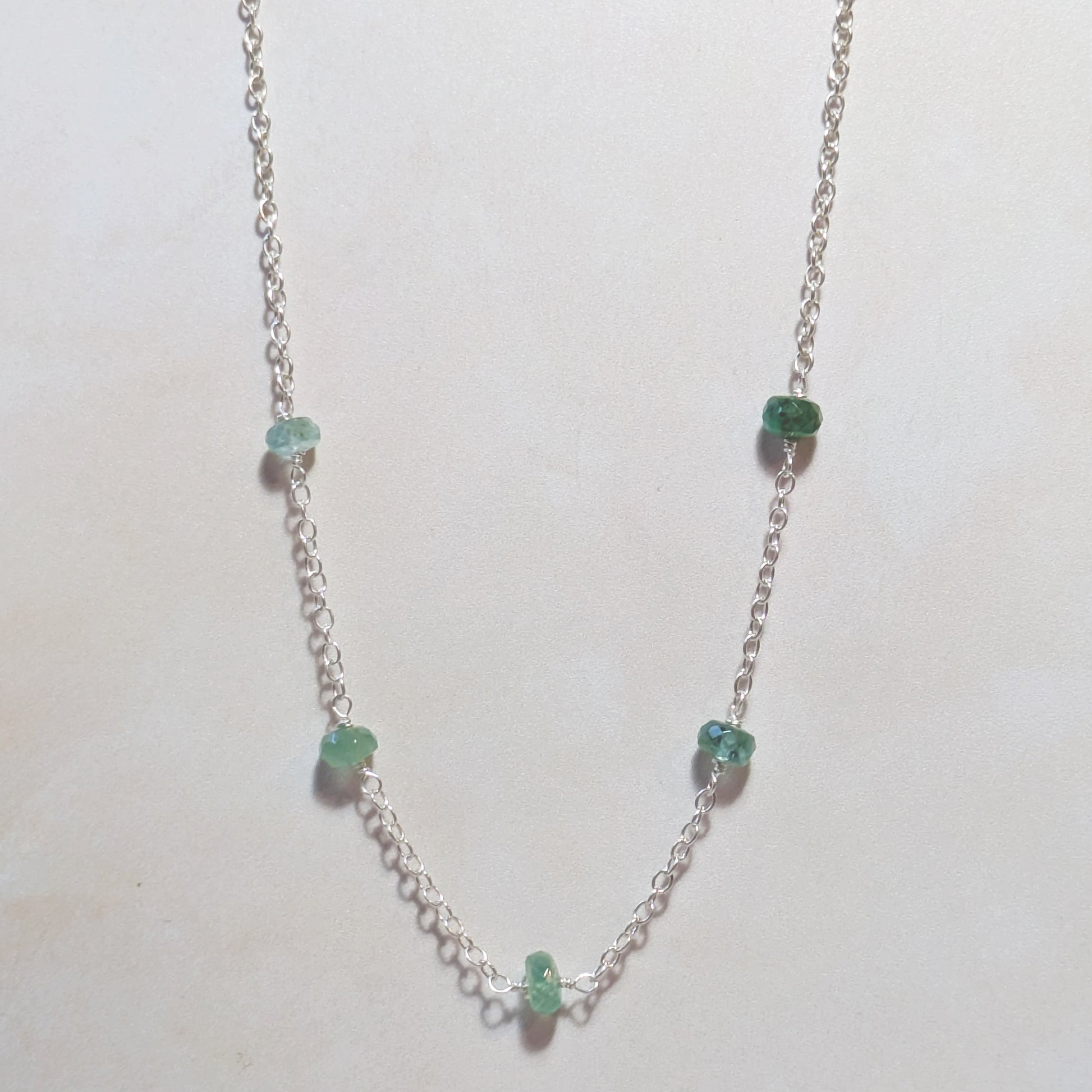 Silver necklace with green Emerald gemstones on a white background.