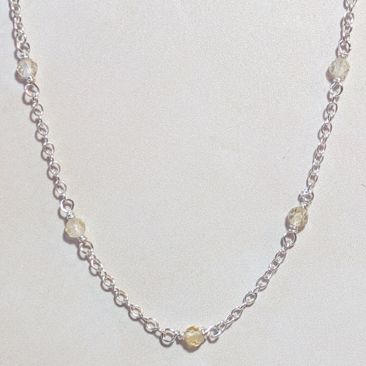 Silver chain necklace with small Citrine gemstone beads on a neutral background.