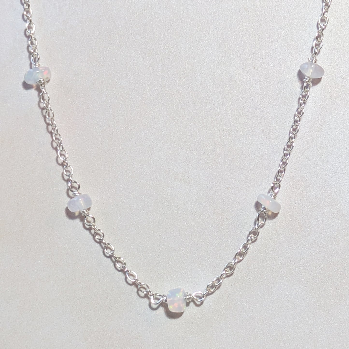 Silver chain necklace with opal beads on a light neutral background.
