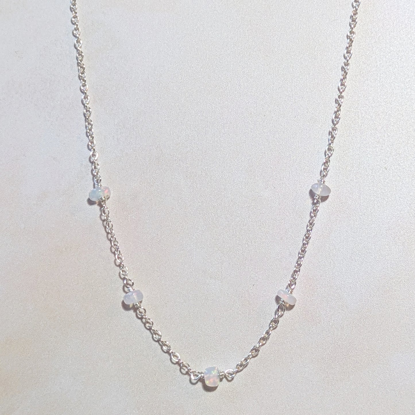 Silver necklace with Opal gemstone beads on a light gray background.