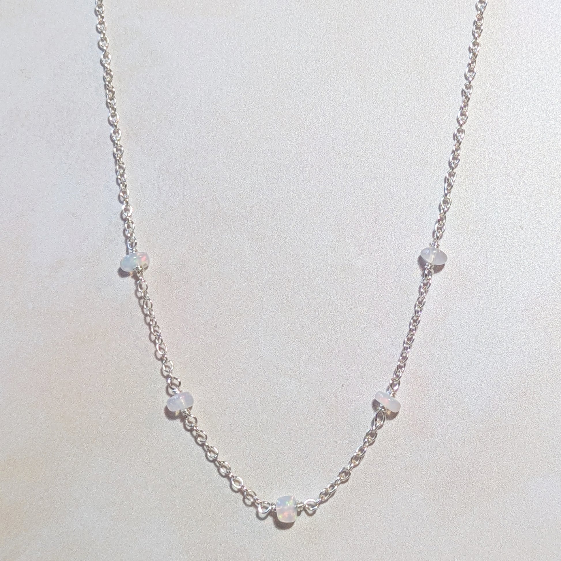 Silver necklace with Opal gemstone beads on a light gray background.