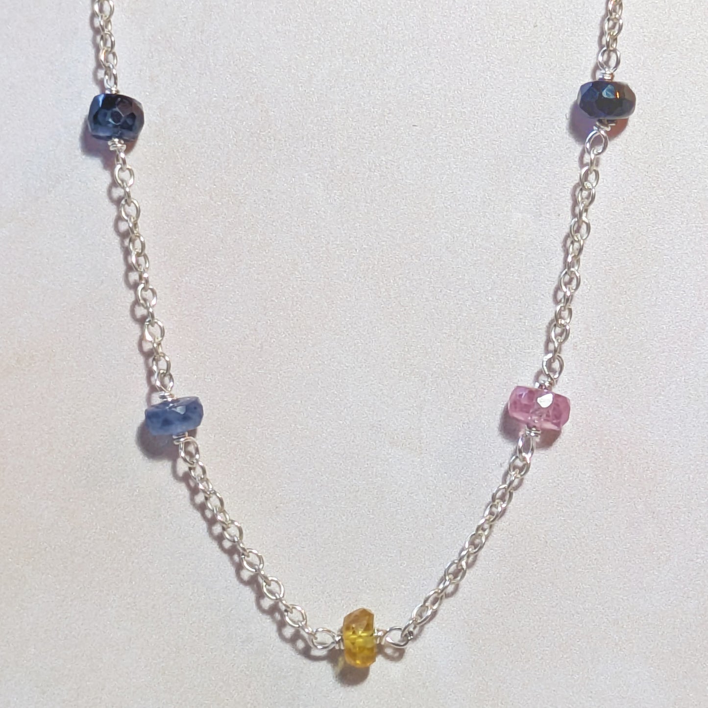 Silver chain necklace with multicoloured Sapphire beads on a white background.