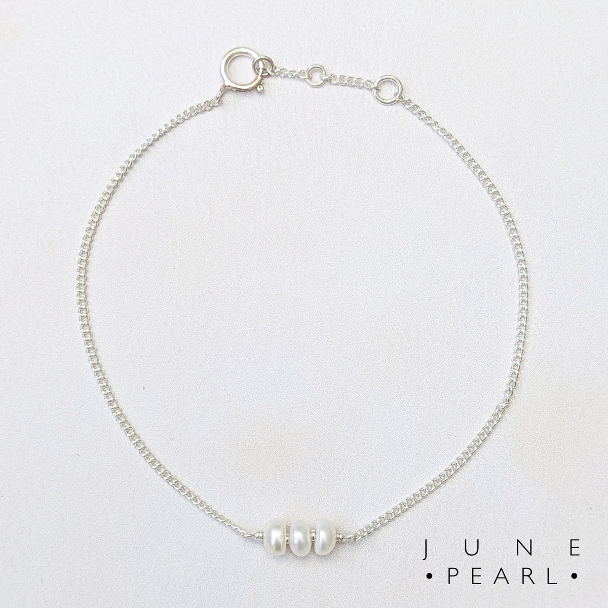 A delicate silver birthstone bar bracelet featuring three small white pearls at the centre, displayed on a clean white background with the text 'JUNE PEARL' printed in the bottom right corner.
