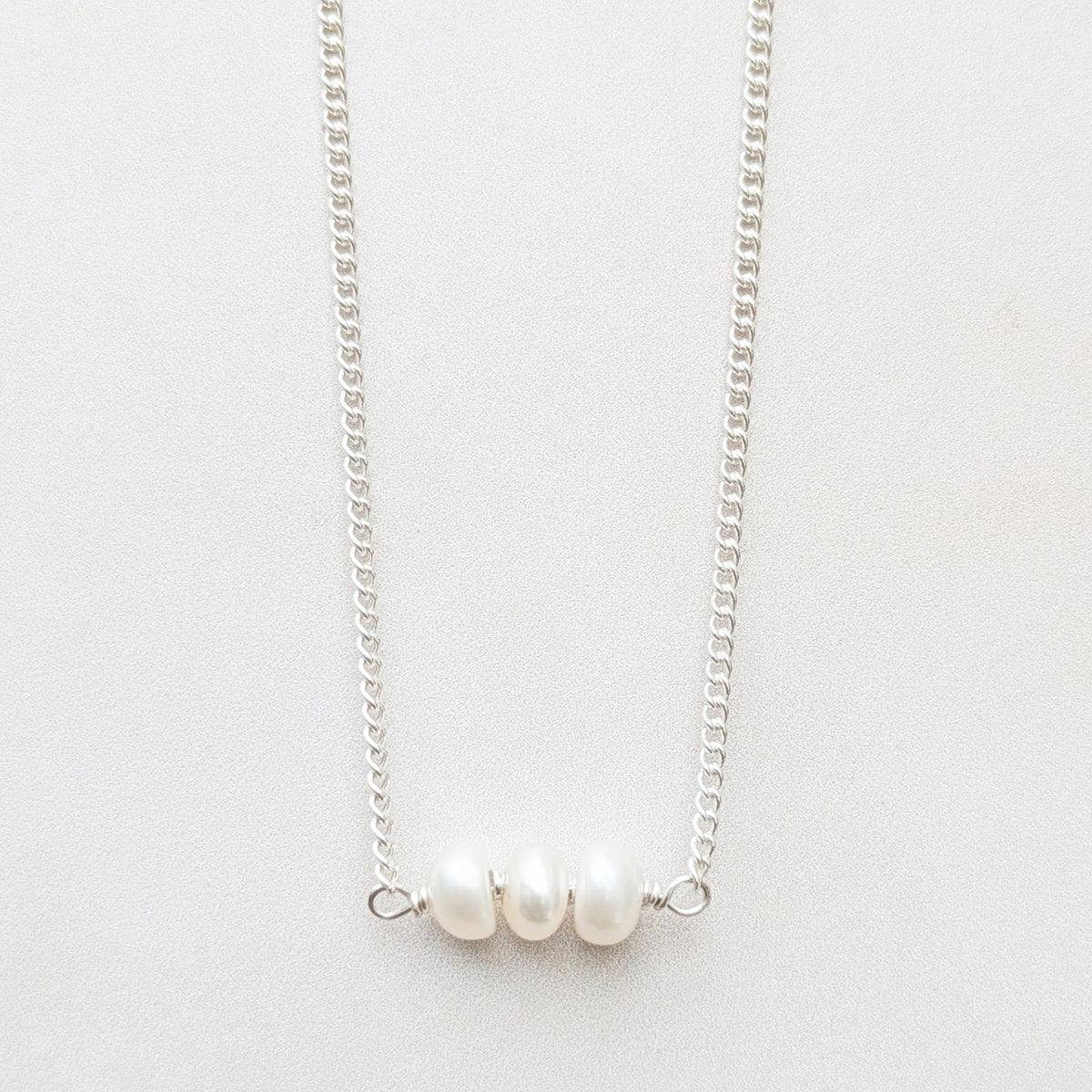 A delicate recycled silver birthstone bar necklace featuring three small, lustrous white pearls aligned horizontally on a plain light background.