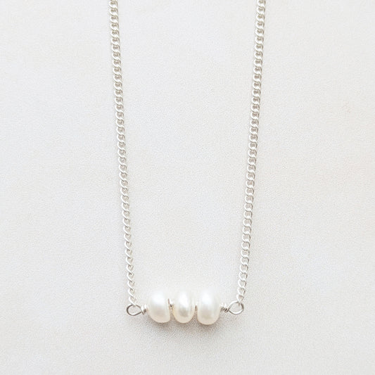 A delicate recycled silver birthstone bar necklace featuring three small, lustrous white pearls aligned horizontally on a plain light background.