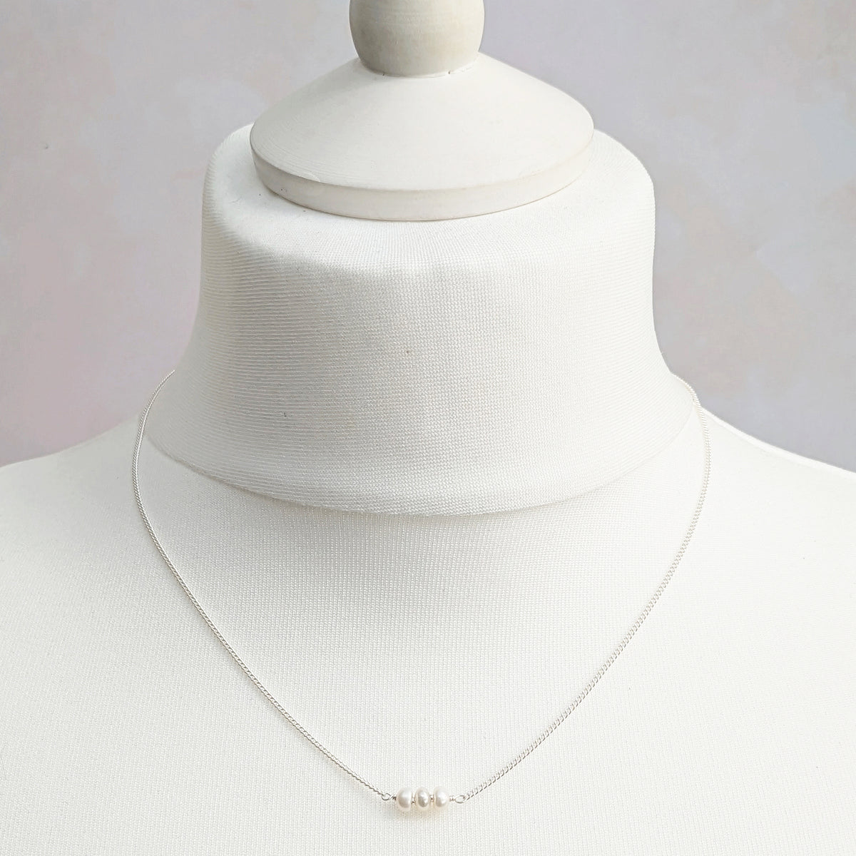 A silver curb chain necklace with three small white pearls at the centre, displayed on a white fabric mannequin bust.